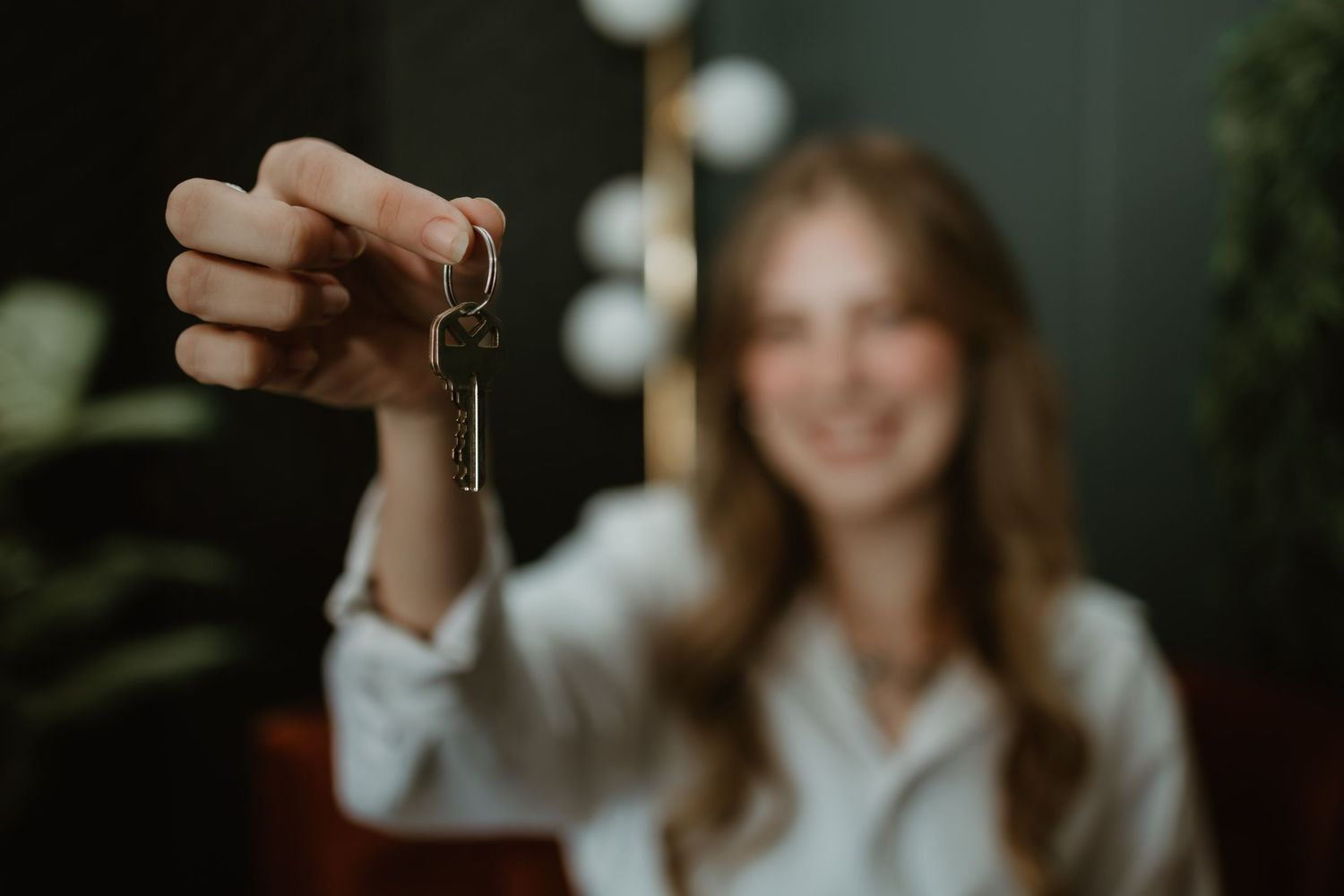 Hand holding up an old key against a blurred interior background with soft bokeh lighting effect.