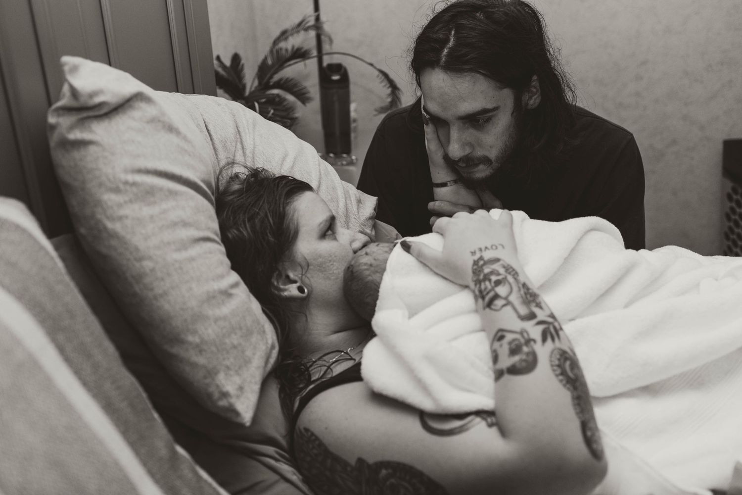 A black and white photograph shows two people in what appears to be a hospital or medical setting with pillows and blankets.