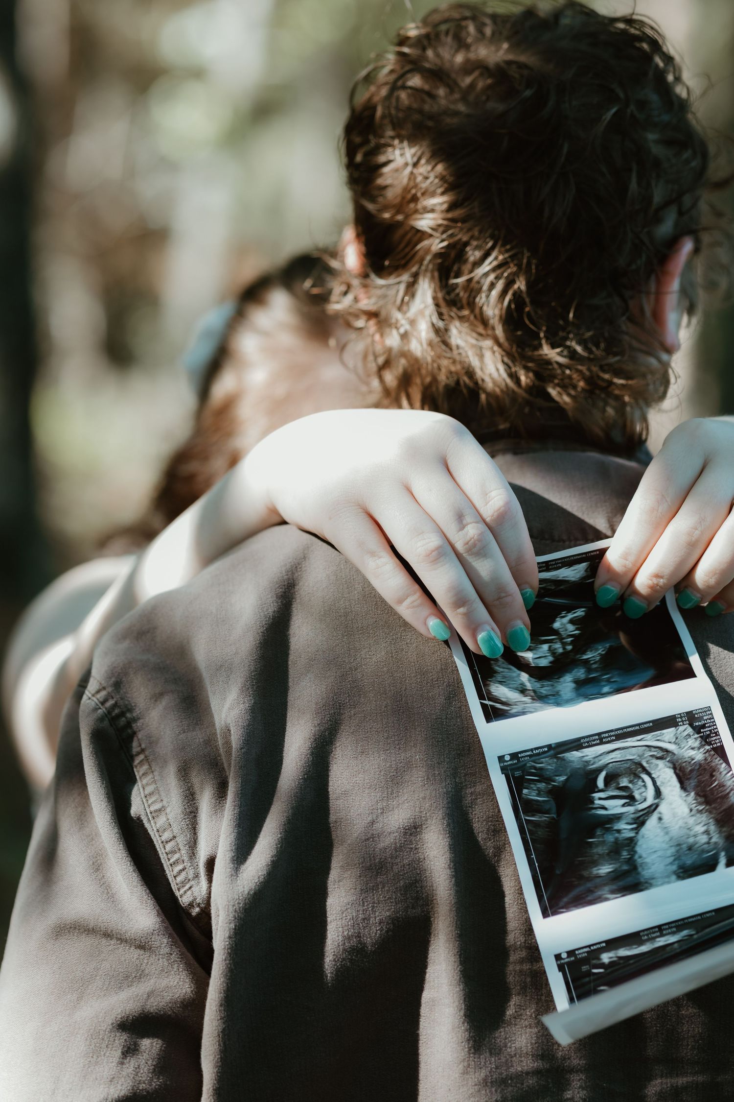 Someone holding an ultrasound photo over their shoulder while wearing a brown jacket.