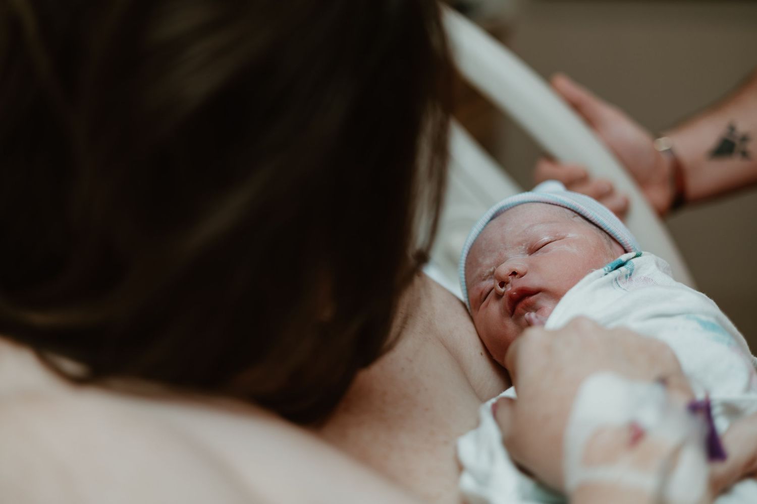 A newborn baby rests peacefully against someone's chest during skin-to-skin contact in a hospital setting.