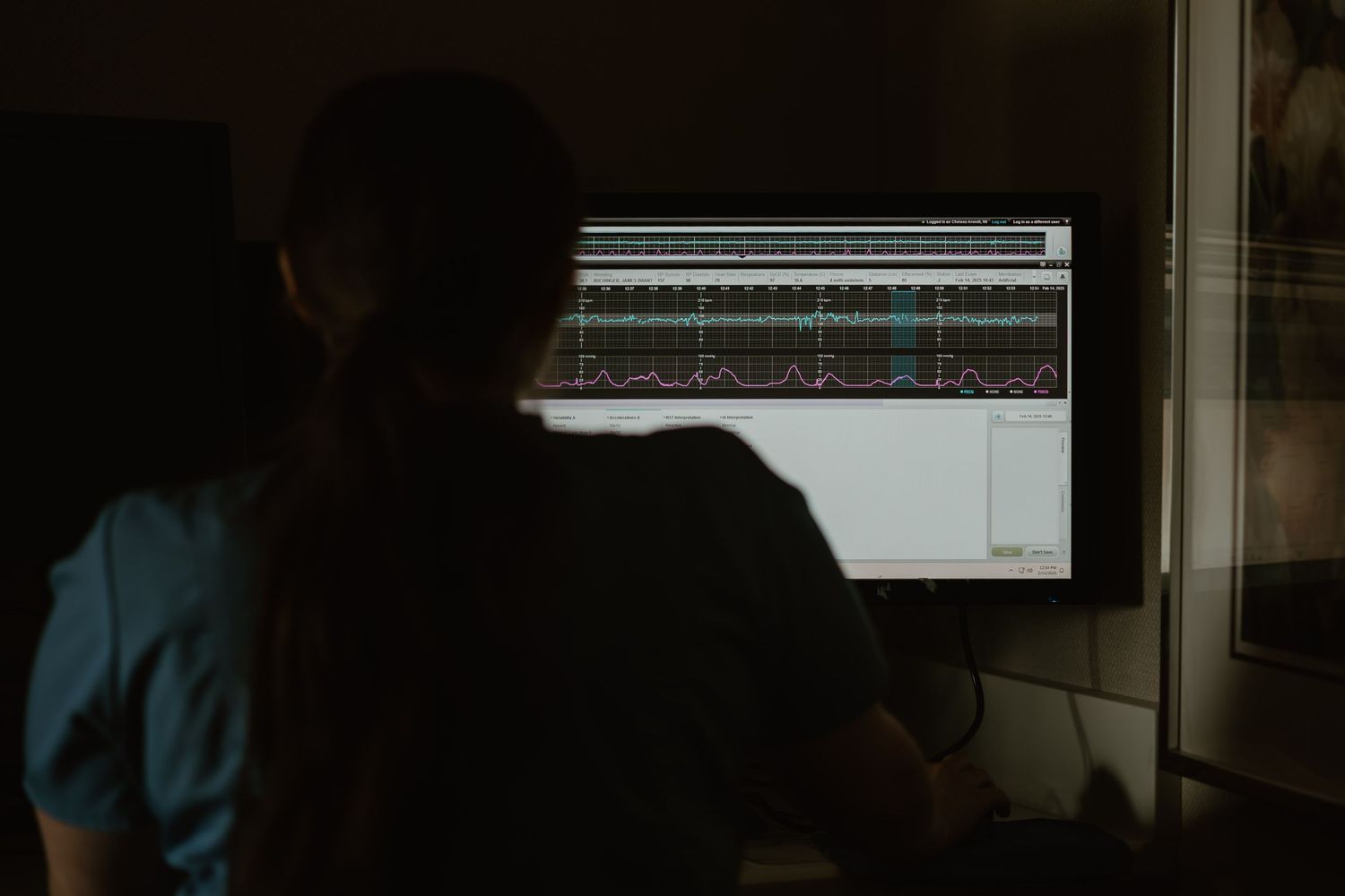 Someone working on a digital audio workstation in a dark room with glowing computer screen showing audio tracks.