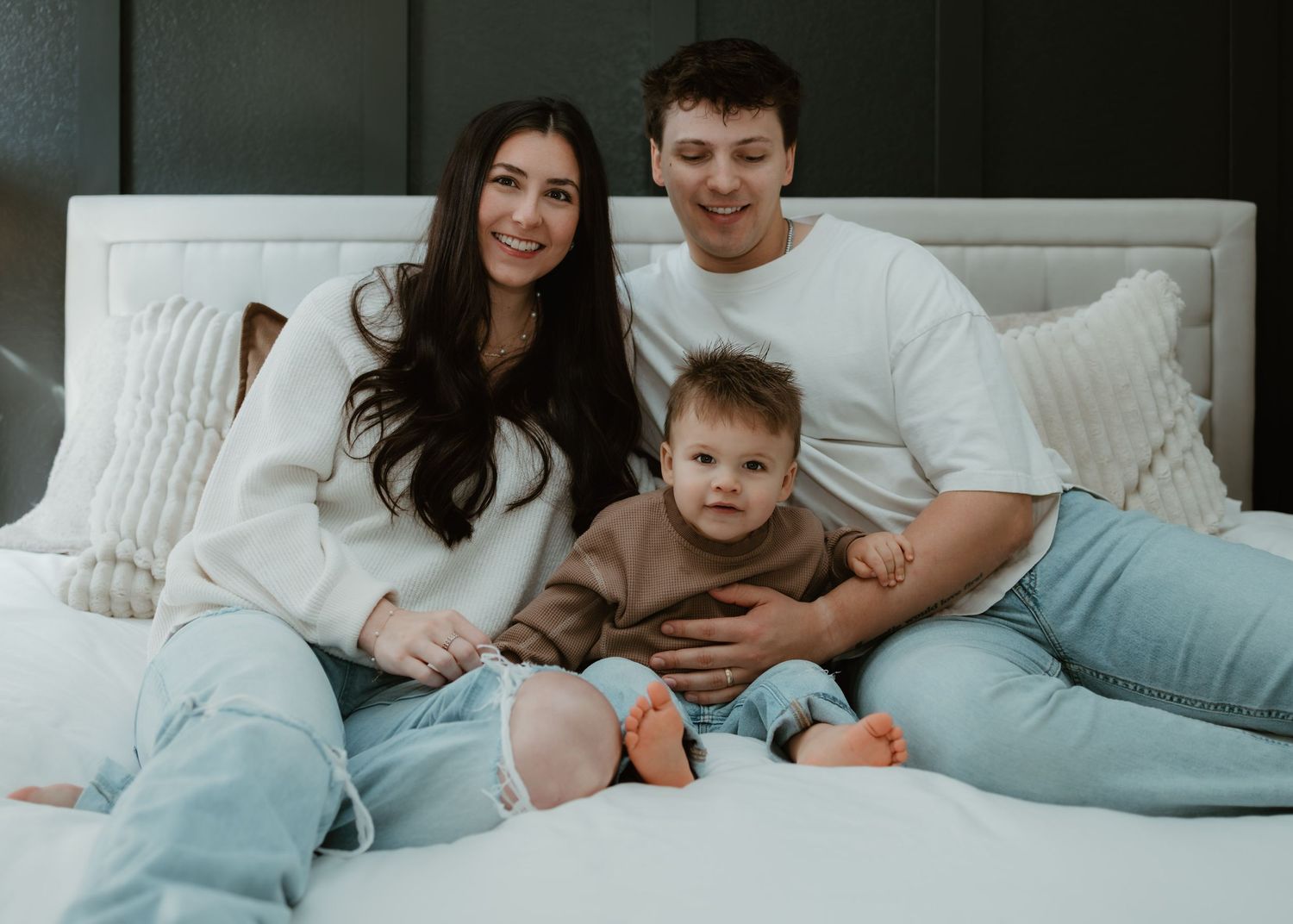 Relaxed family lying together on cozy bedding while looking at mobile device in bedroom.