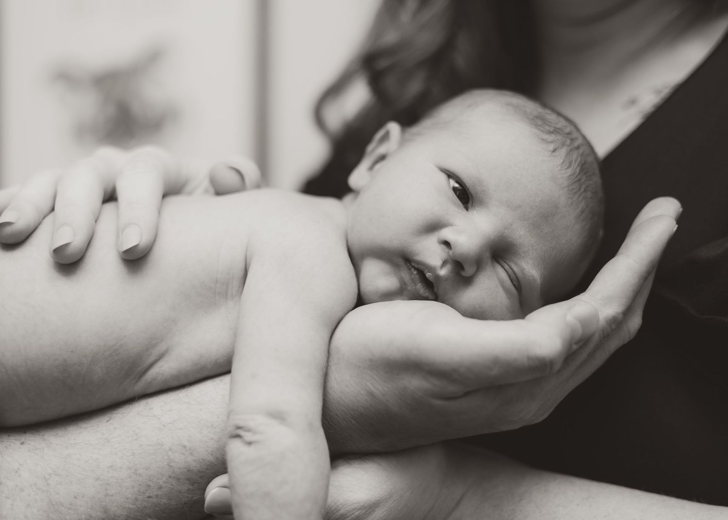 A black and white close-up image of a sleeping baby's hand gently resting on a soft surface.