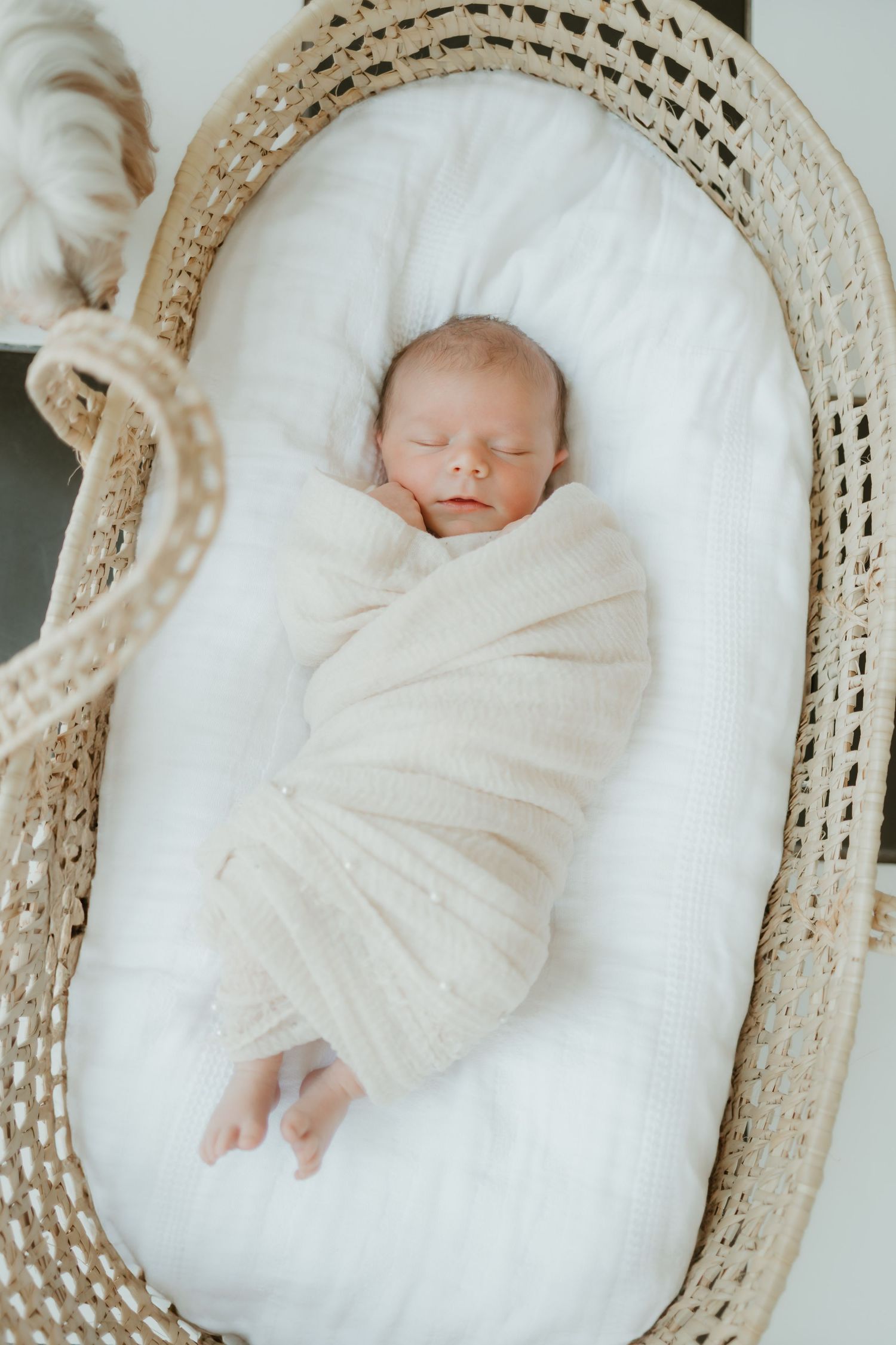 Baby peacefully sleeping in a white cozy bassinet with a woven frame and soft white blanket.