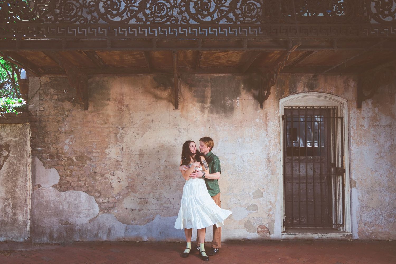 Couple sharing a romantic kiss outdoors near a rustic stone wall and wooden door.