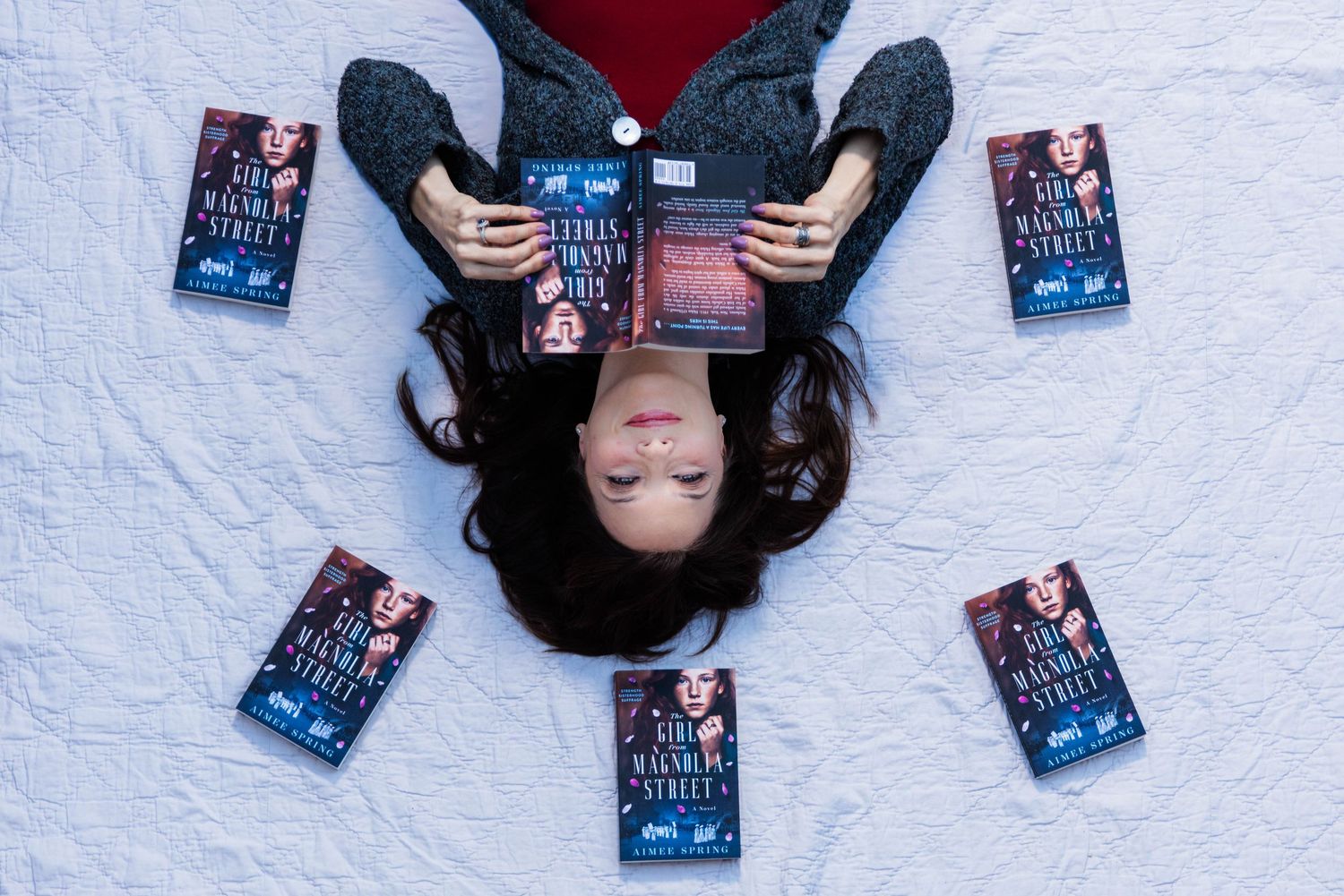 A person lies on a white surface surrounded by multiple copies of a book in a creative overhead photo composition.