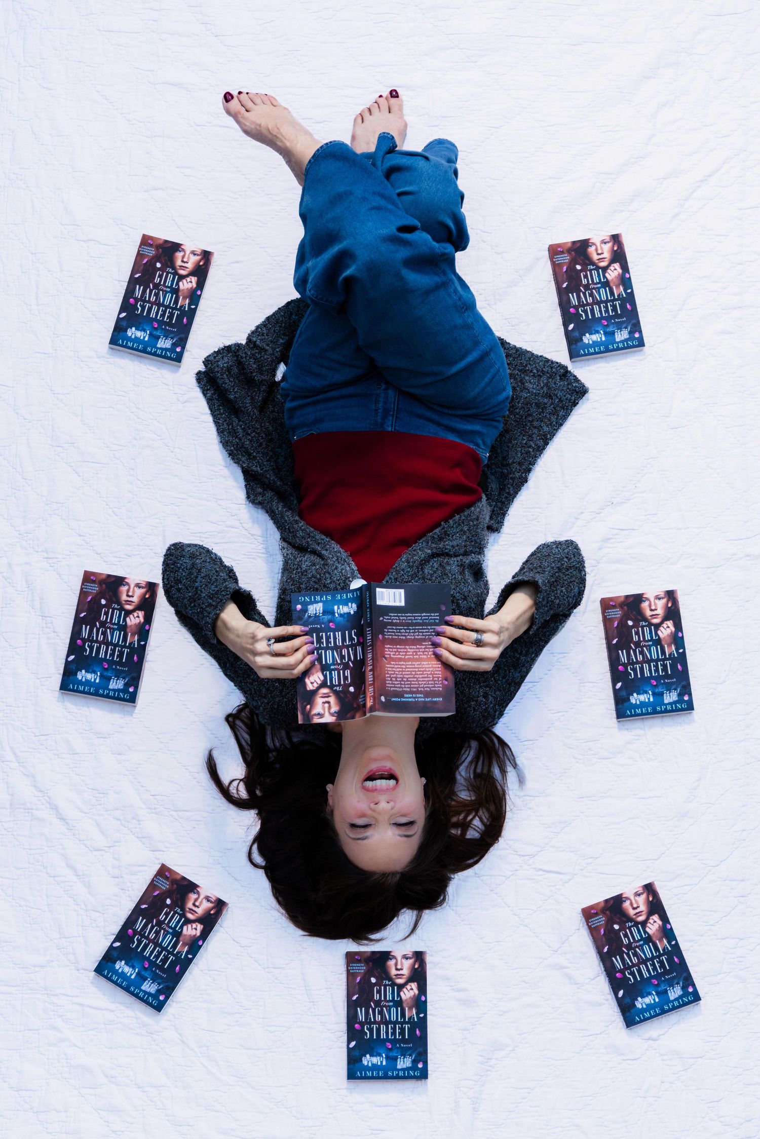 Person lying on white background surrounded by blue book covers in creative promotional photo series.