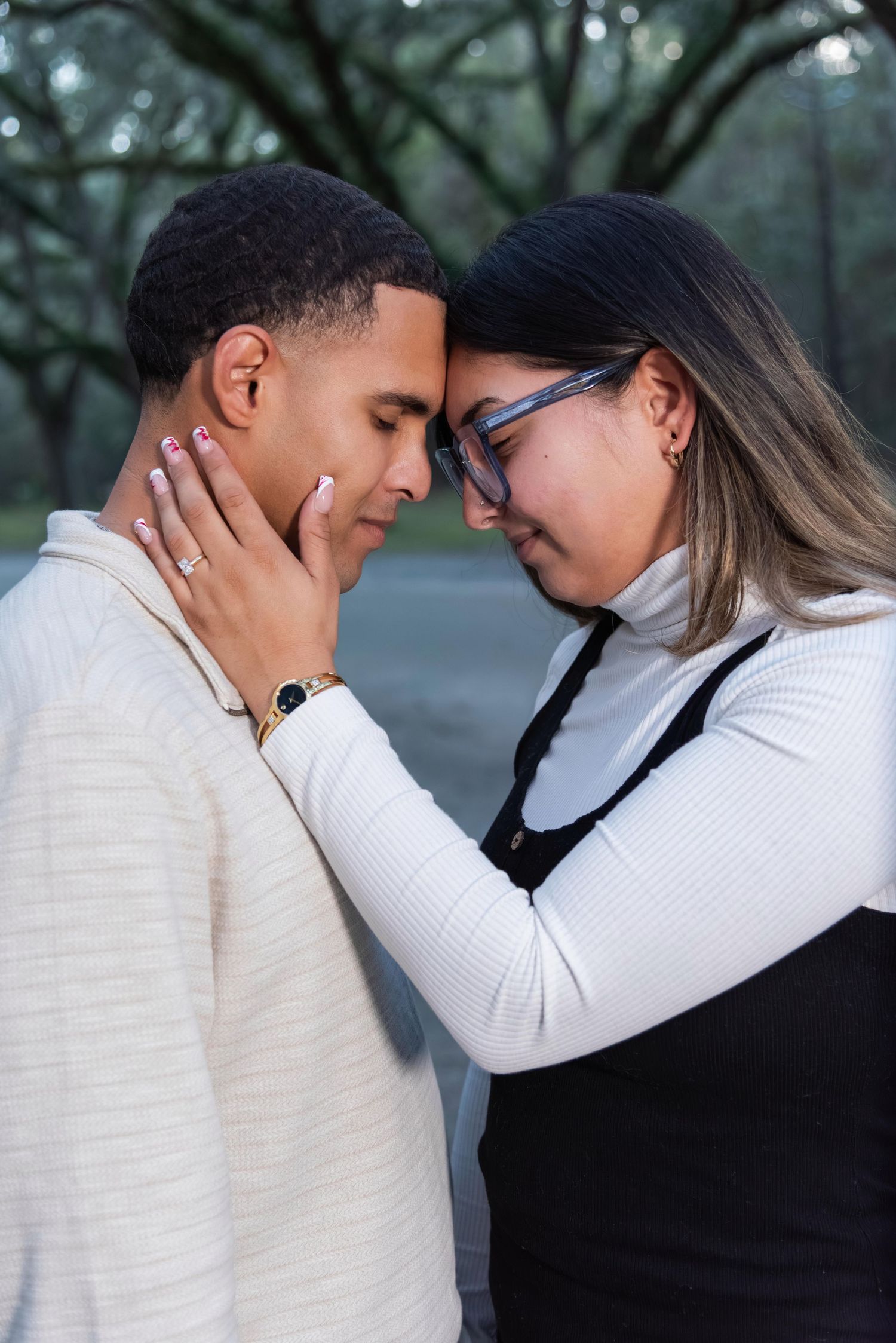 Couple sharing an intimate moment, touching foreheads outdoors, woman in black overalls holding mans face gently.