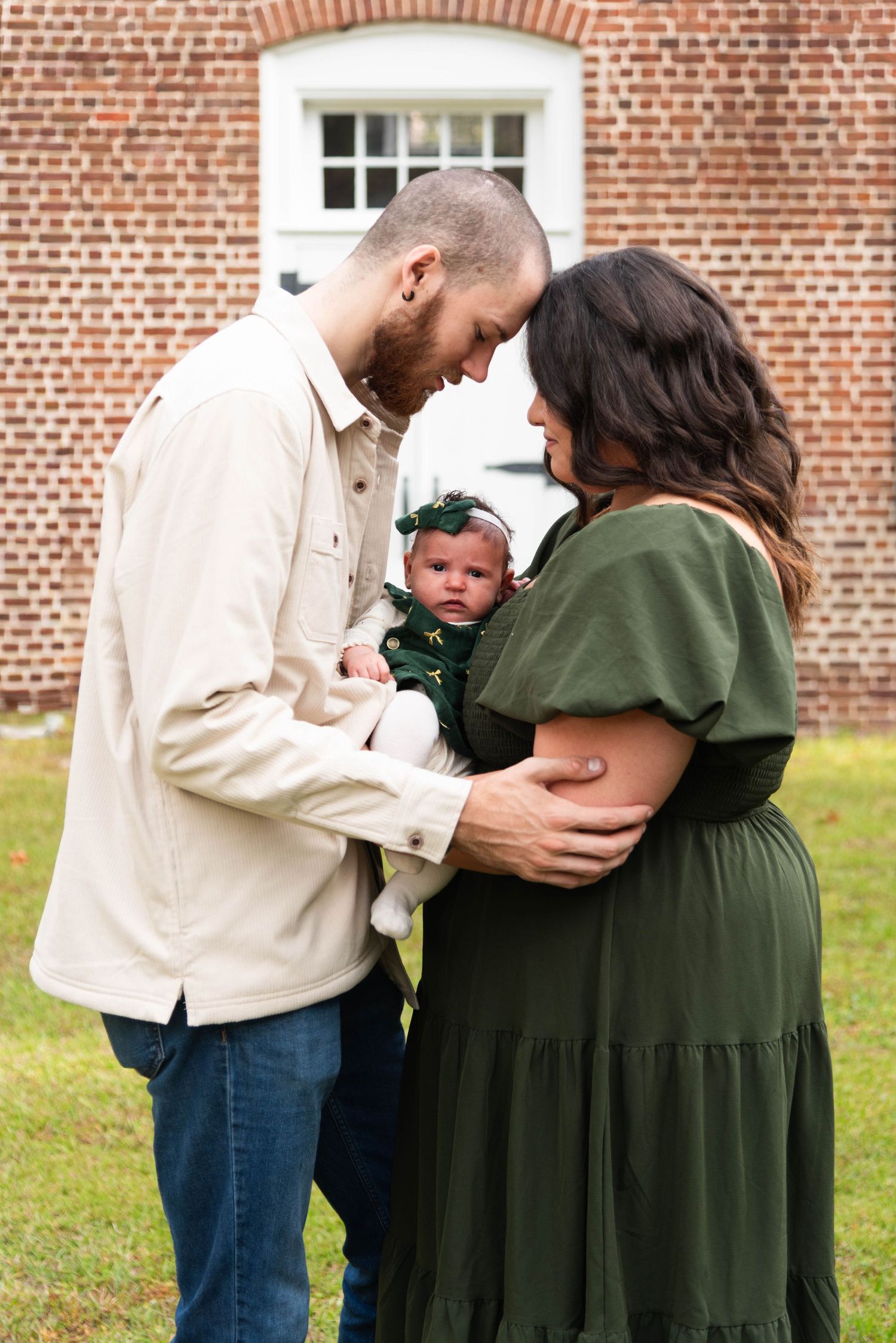 A couple in casual attire sharing an intimate moment with their baby against a brick building backdrop.