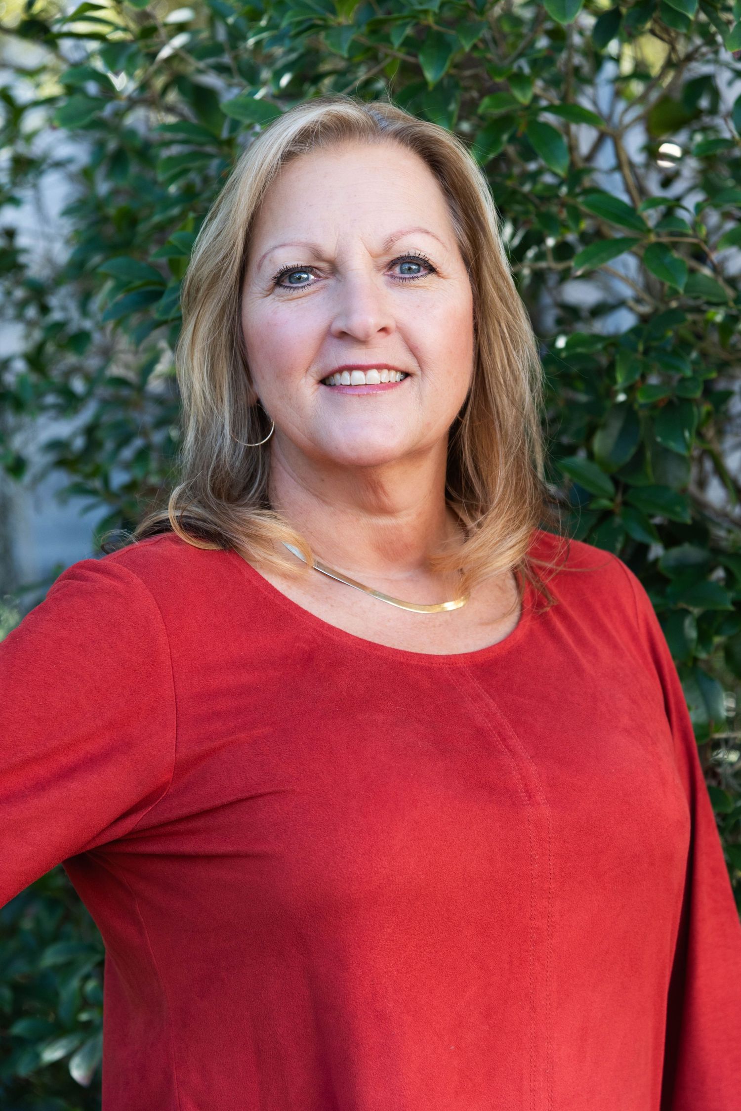 A series of close-up portrait photos of someone in a red sweater smiling against a green leafy background.