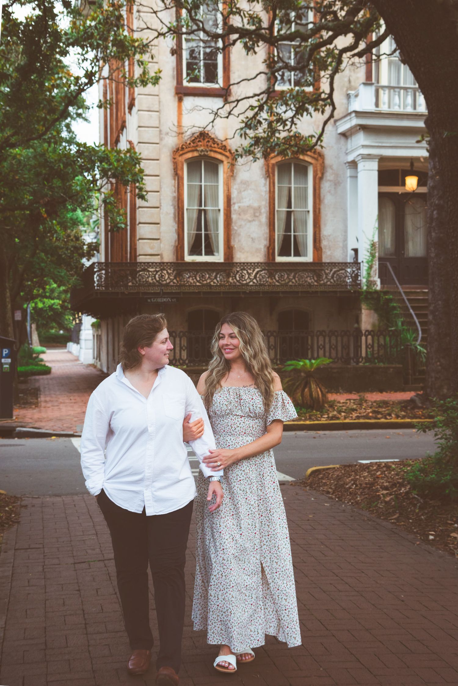 Two women walking together in front of a historic building with ornate balcony in Savannah, GA.