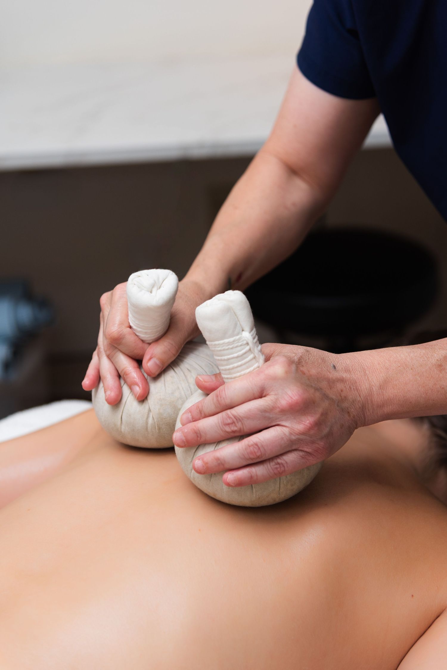 Massage therapist performs a therapeutic treatment using warm herbal compress balls on client's back.