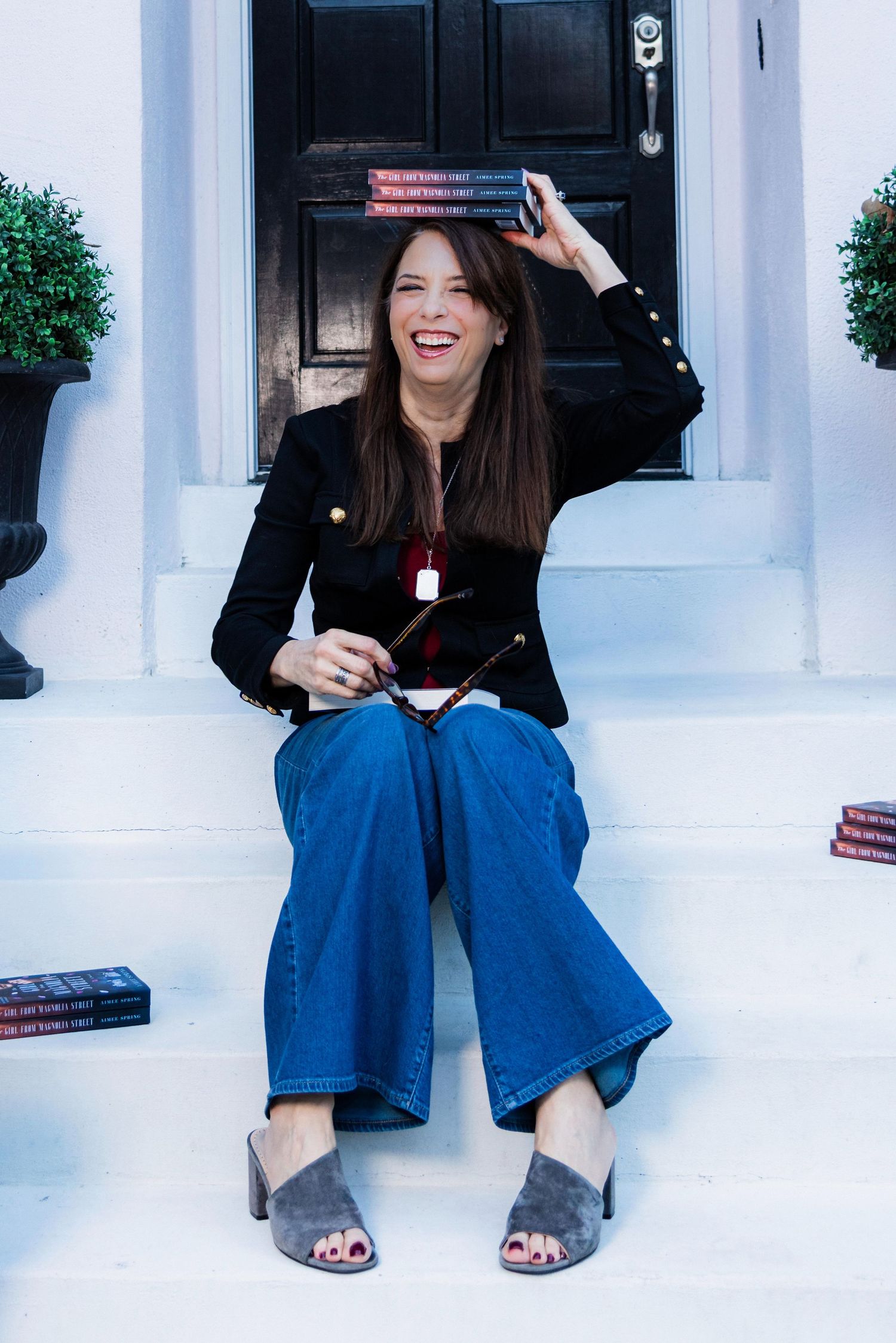 A person in a black top and wide-leg blue jeans sits and laughs on white steps in a casual photo series.