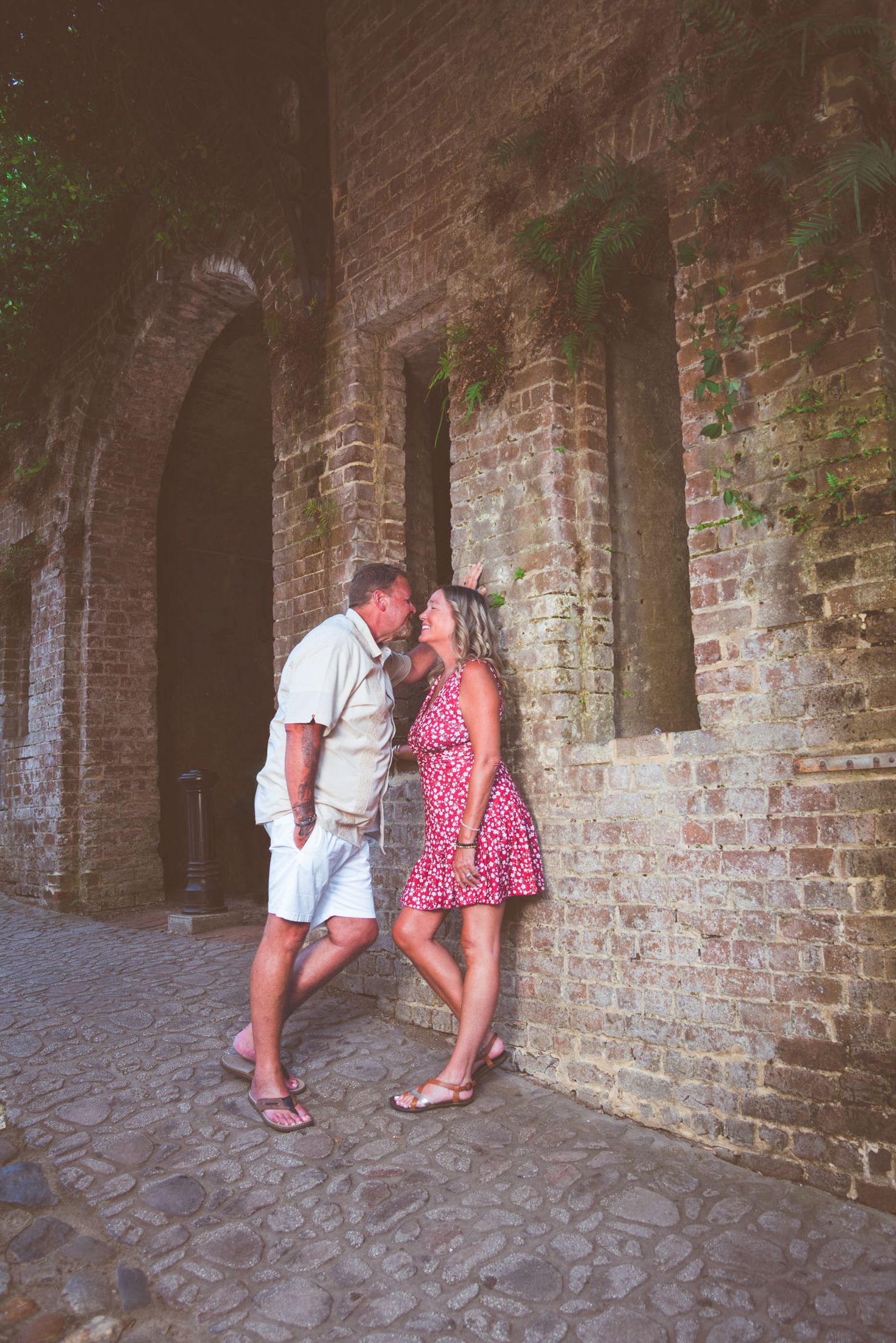 Romantic couple sharing a kiss against an ancient brick wall with arched windows on a cobblestone street.