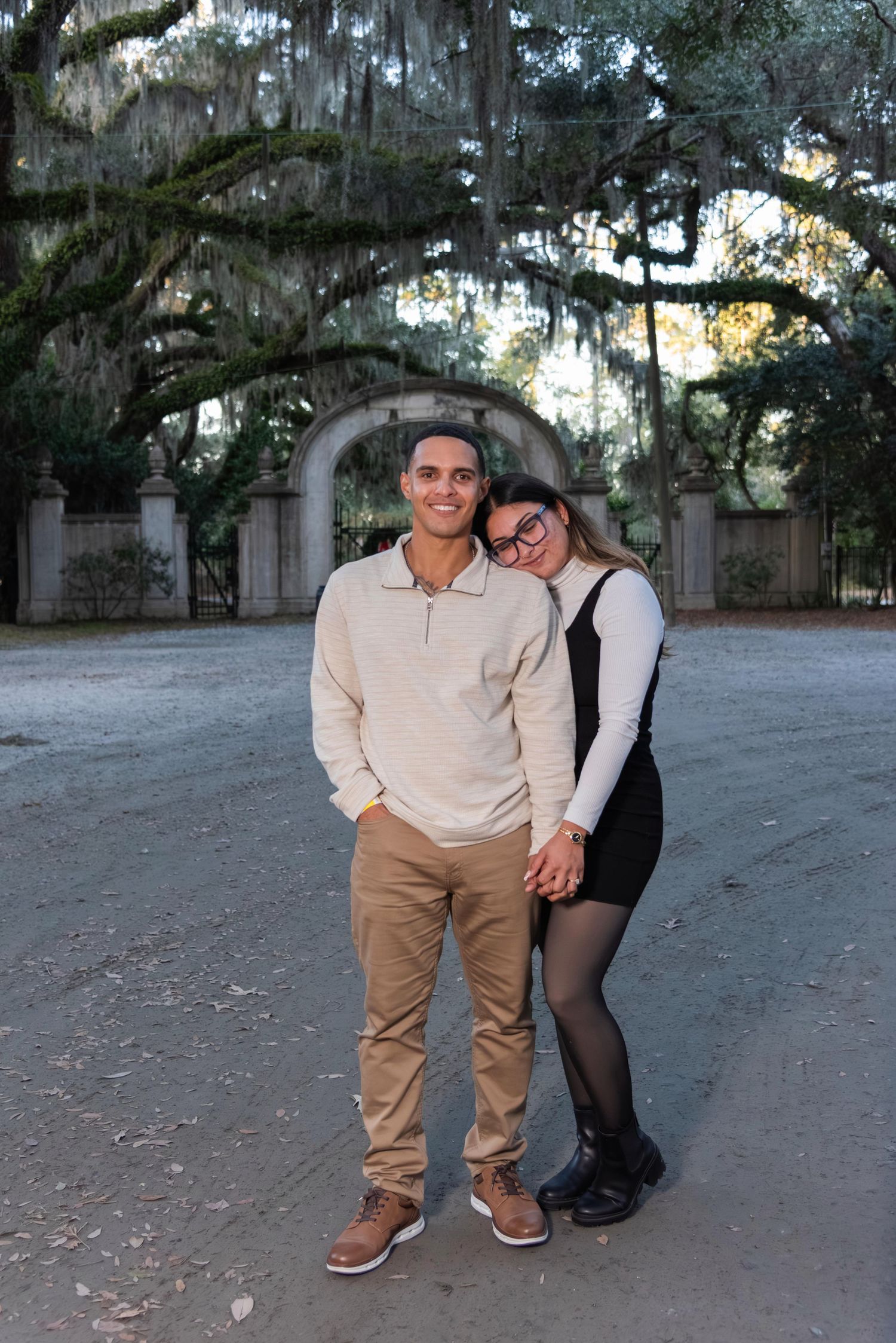 Couple posing together in front of a stone arch with moss-draped oak trees in a scenic outdoor setting.