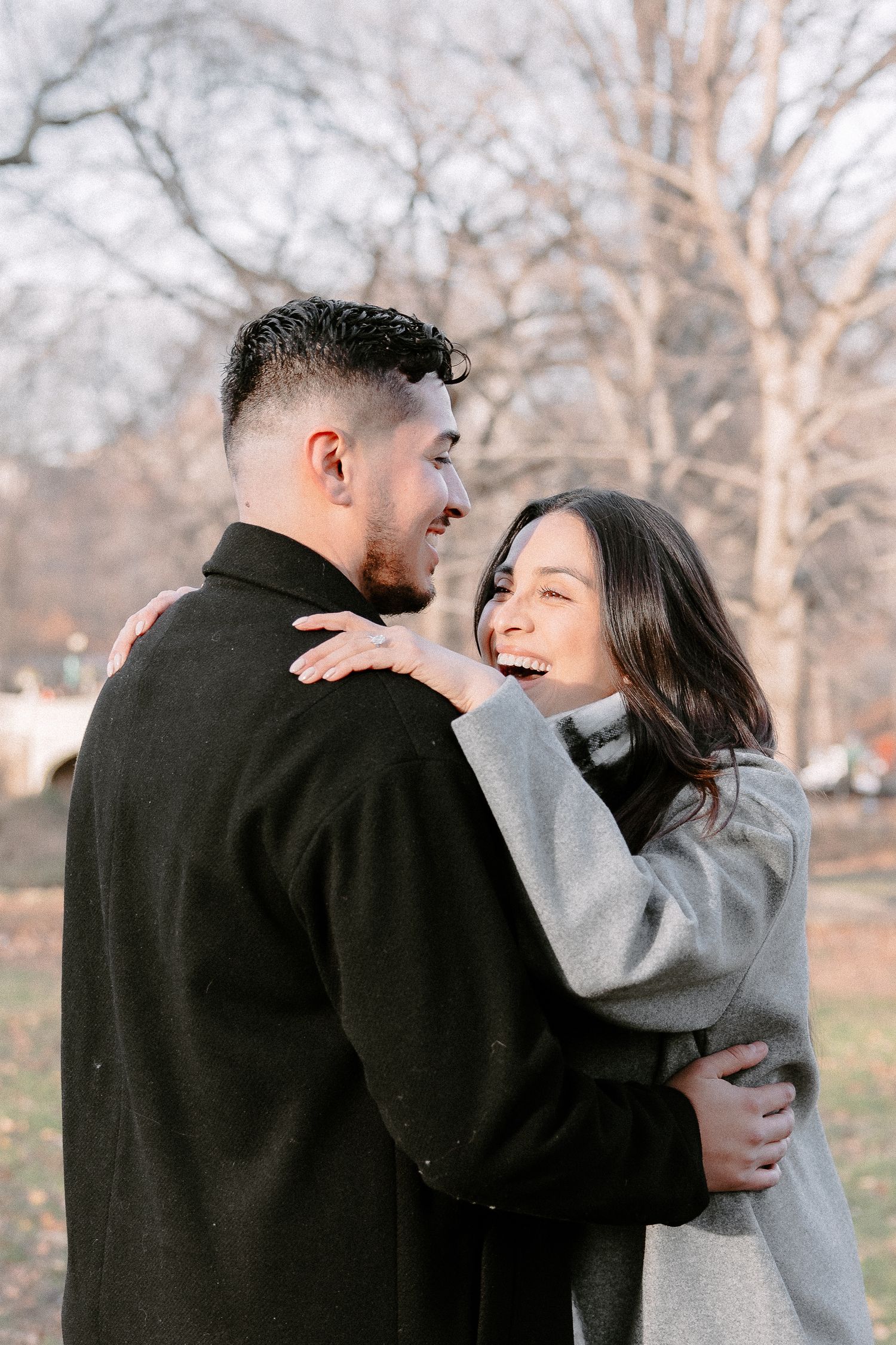 A joyful couple embraces and laughs together outdoors in a park during autumn, wearing stylish coats.
