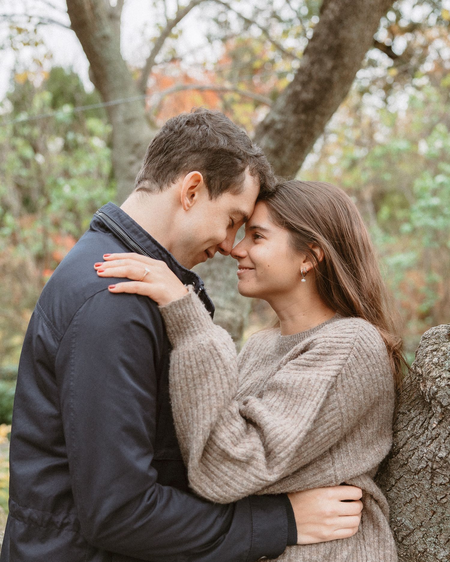 Romantic couple touching foreheads and embracing near a tree in an autumn park setting.