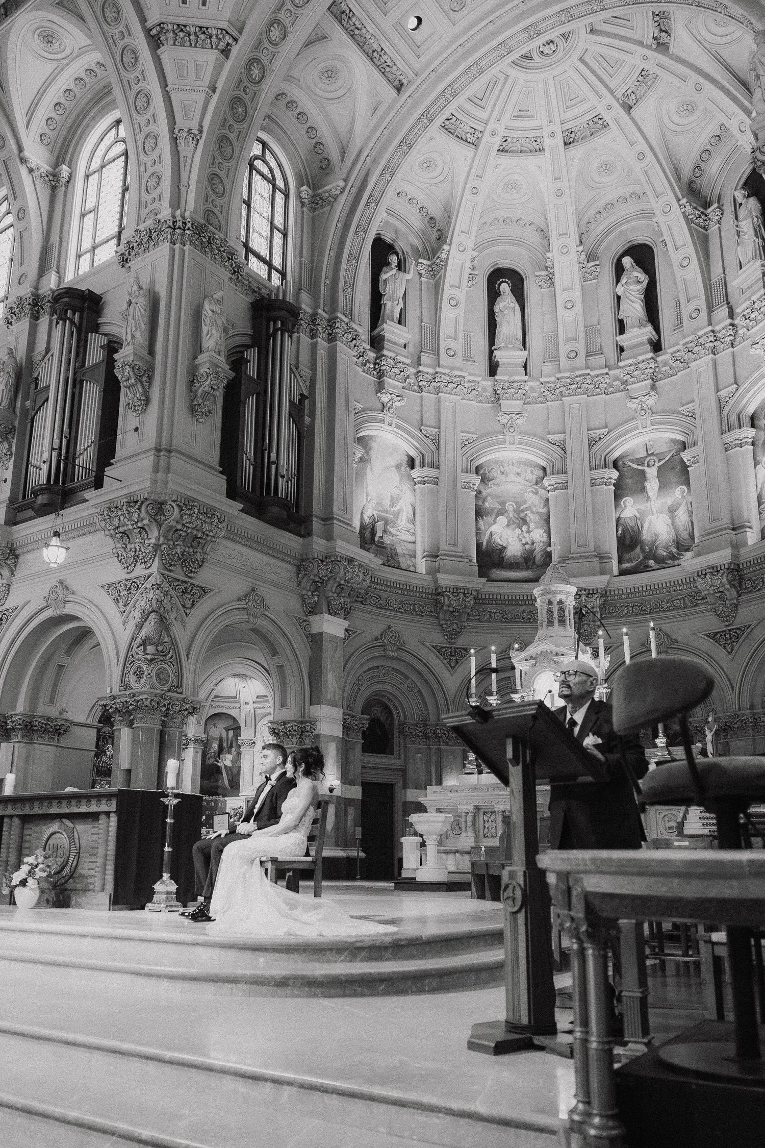 Black-and-white photo of a wedding ceremony inside an ornate cathedral with grand arched ceilings and elegant decor.
