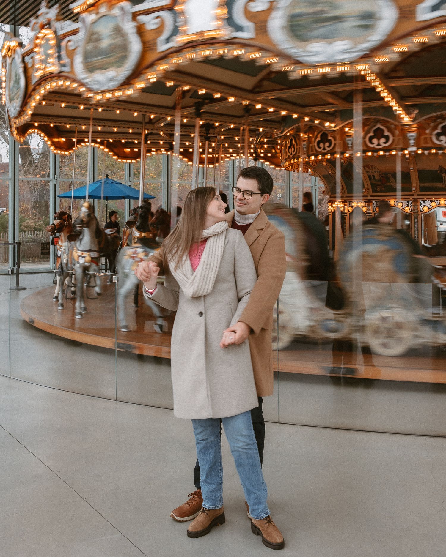 Couple embracing in front of glowing Jane's Carousel in DUMBO Brooklyn at dusk.