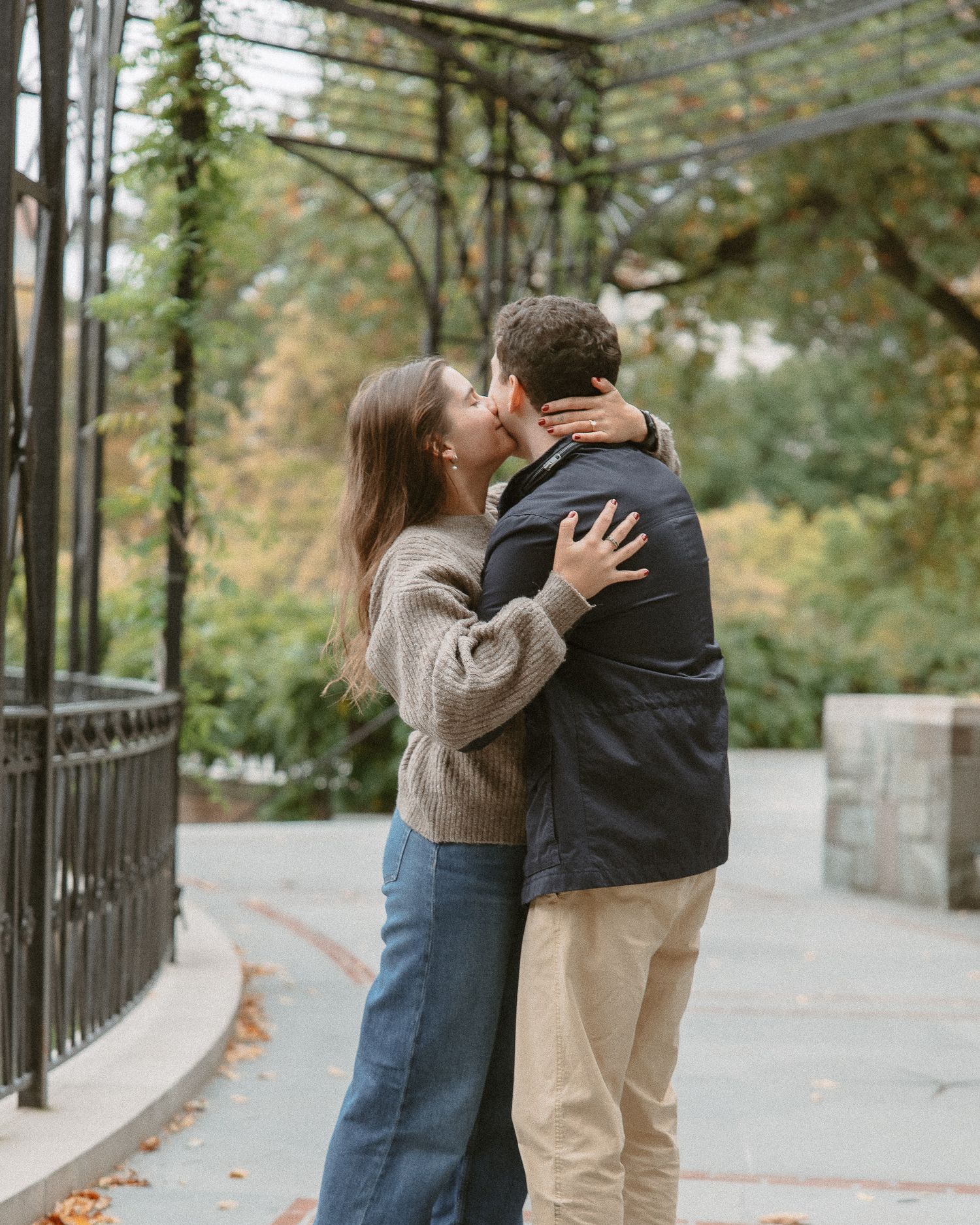 Couple sharing a romantic kiss under an iron pergola in a NYC park.