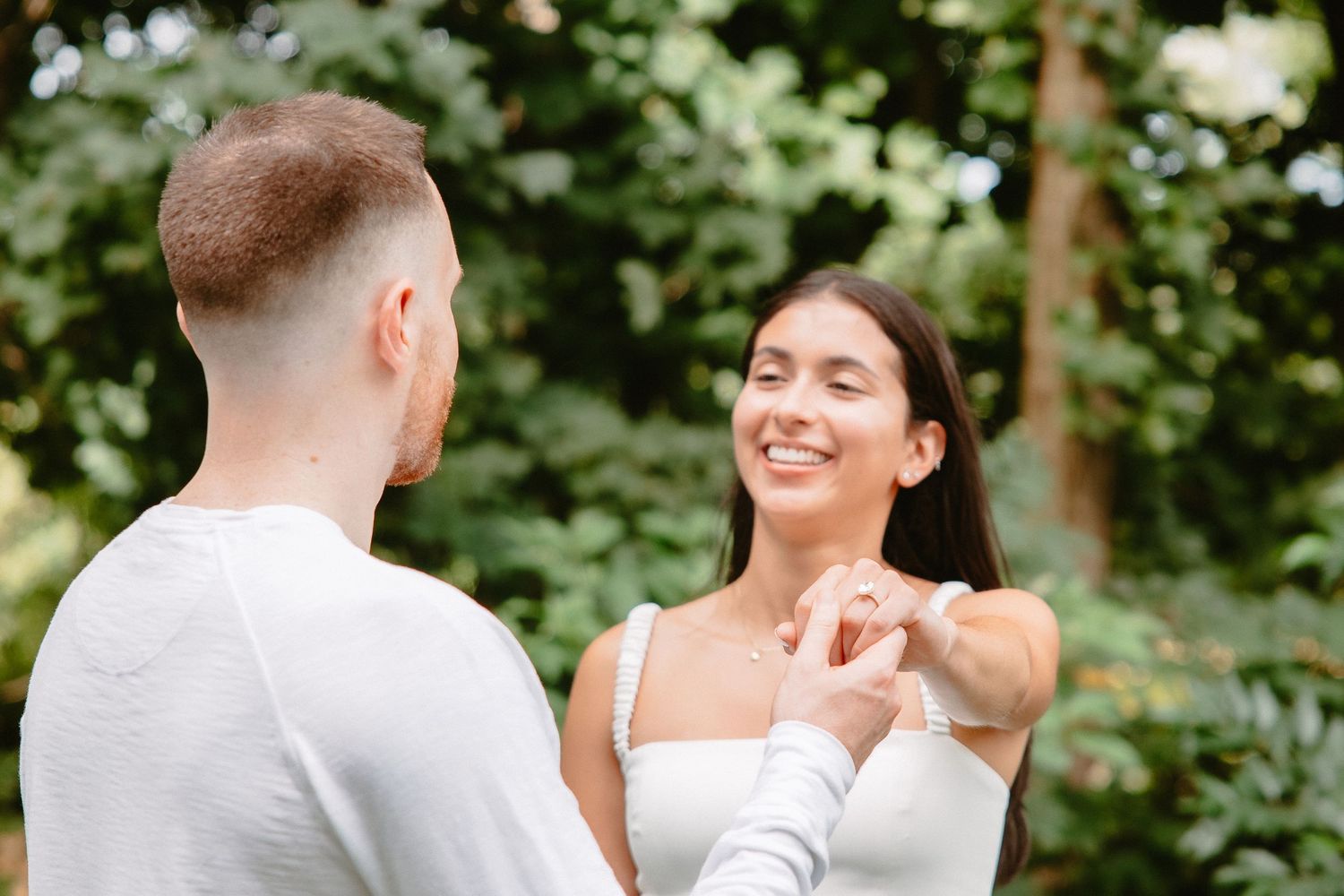 Couple in white outfits holding hands and smiling in a lush green park setting.