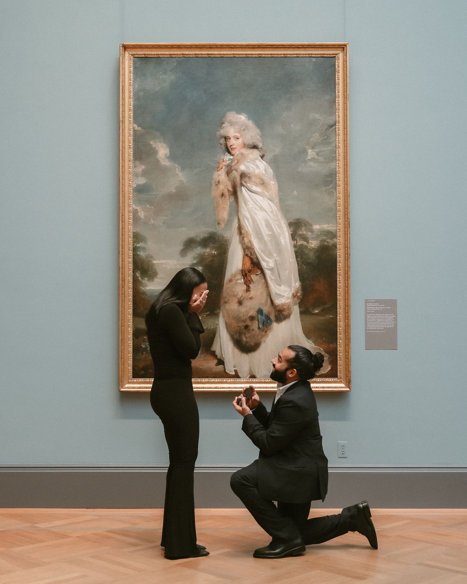 Romantic marriage proposal at museum with man on one knee before elegant classical portrait painting.