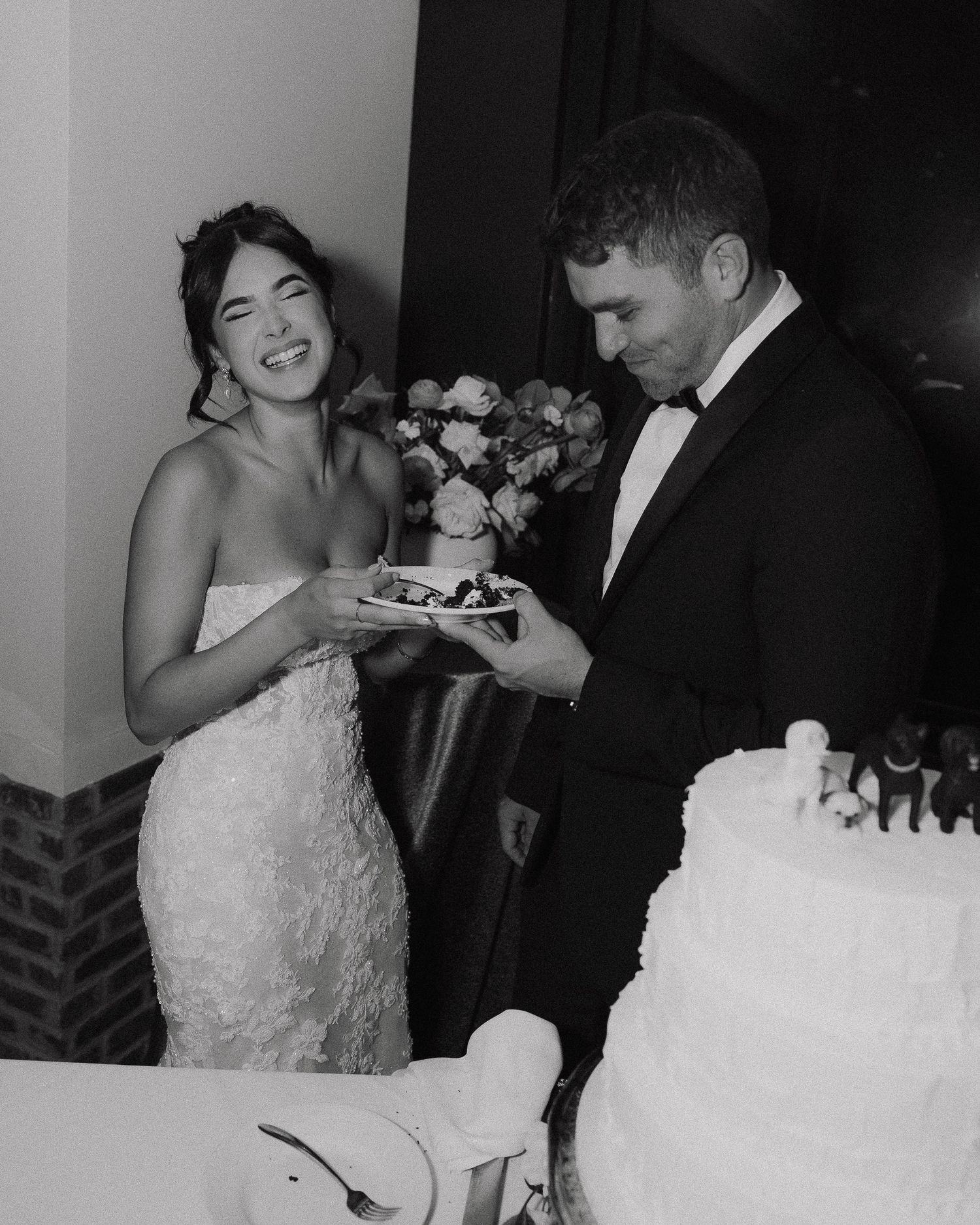 Bride and groom laughing together during wedding cake cutting ceremony at elegant reception.