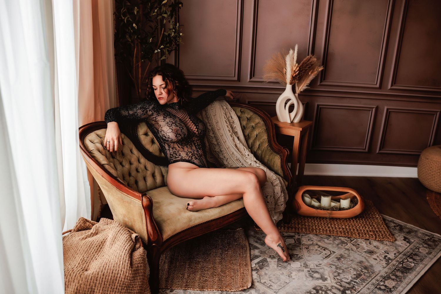 Indianapolis Indiana luxury boudoir portrait of client in fishnet bodysuit sitting on vintage couch with candles