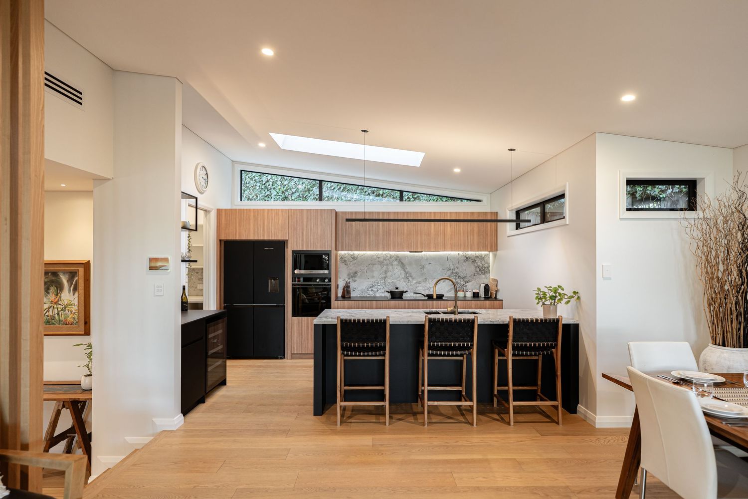 Modern open-plan kitchen with marble backsplash, black island with bar stools, timber floors, and skylight in a luxury home.