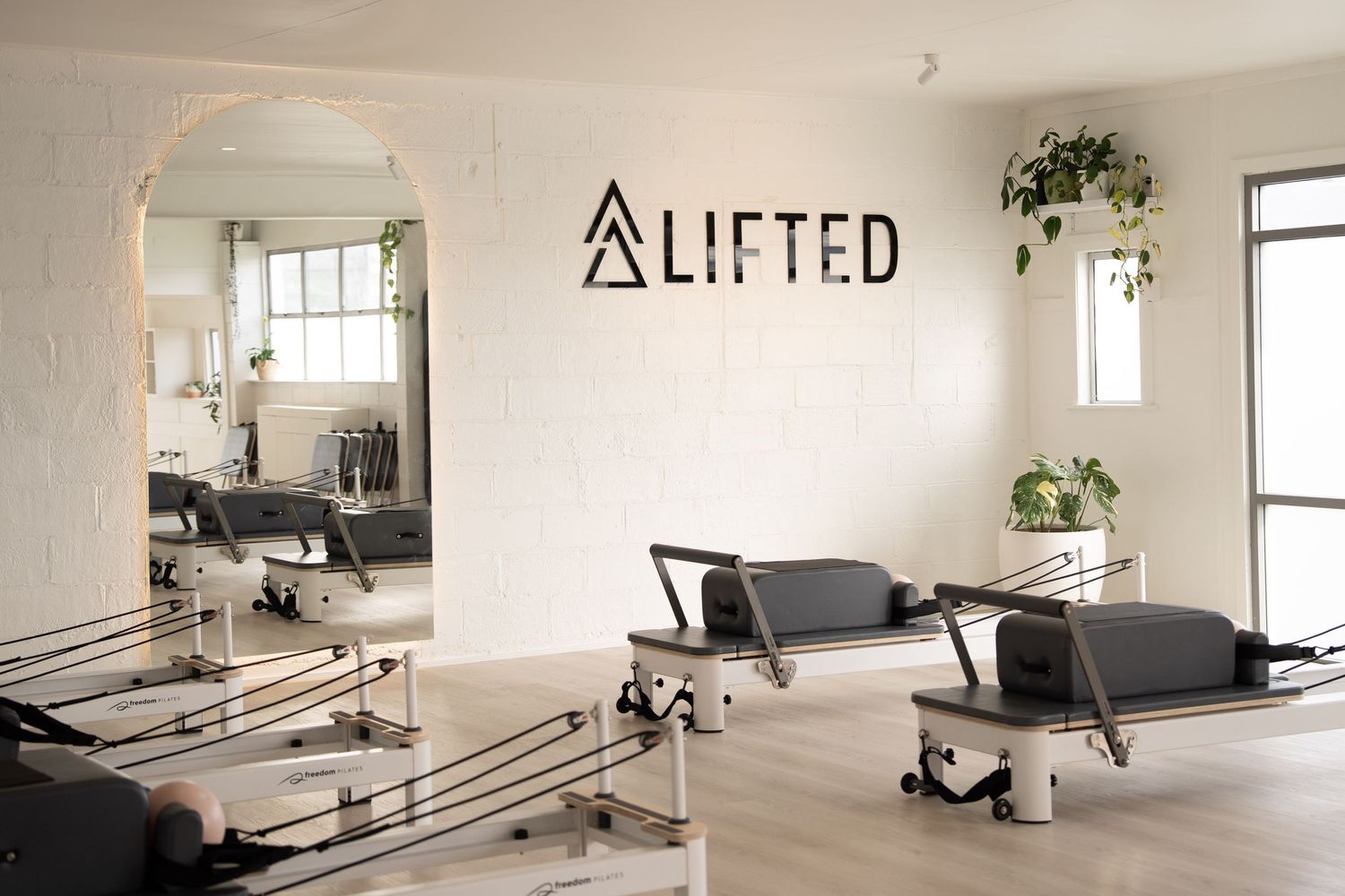 Bright Pilates studio with reformer machines, large mirror, and LIFTED logo on white brick wall.