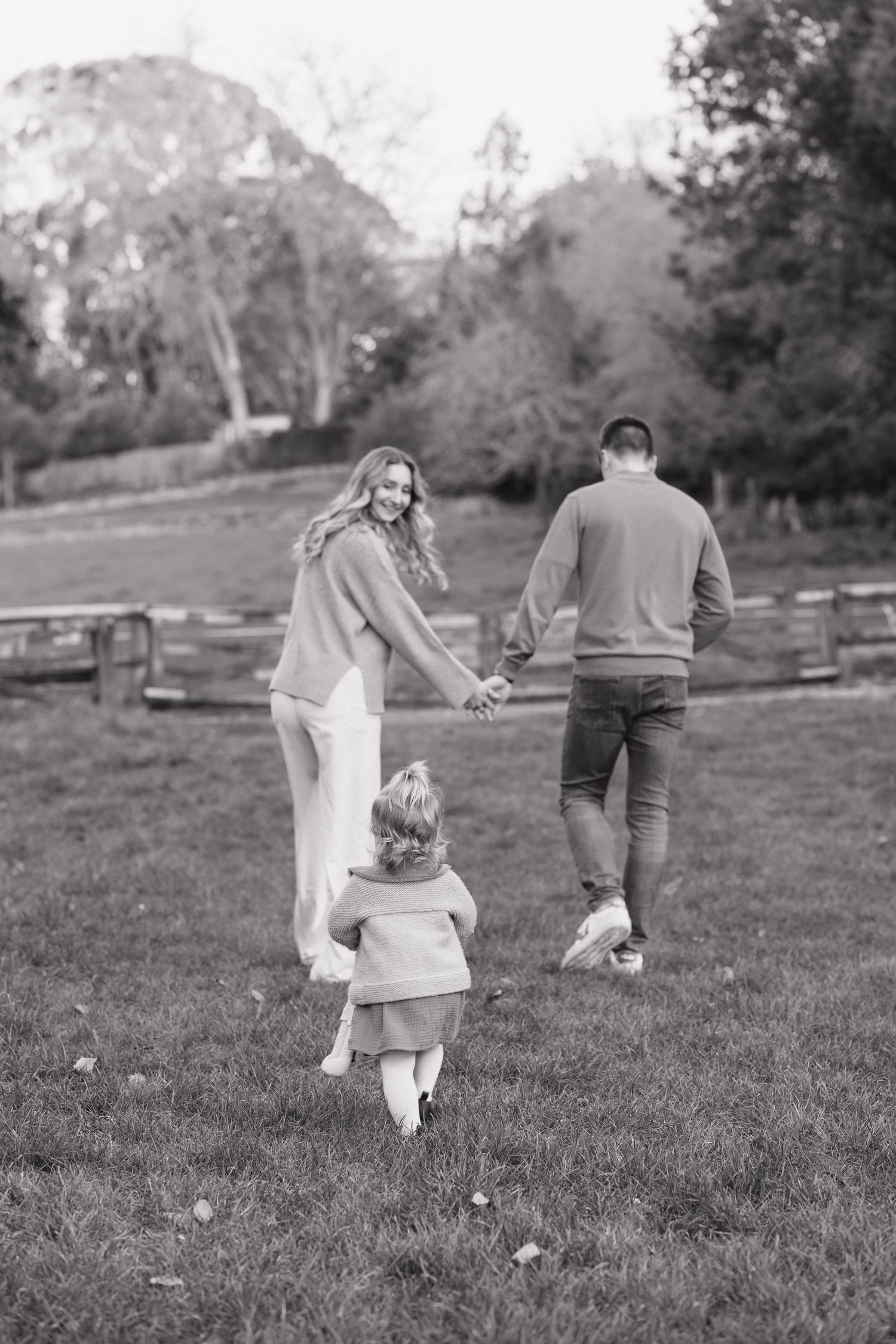Black and white photo of young family holding hands walking across green countryside field.
