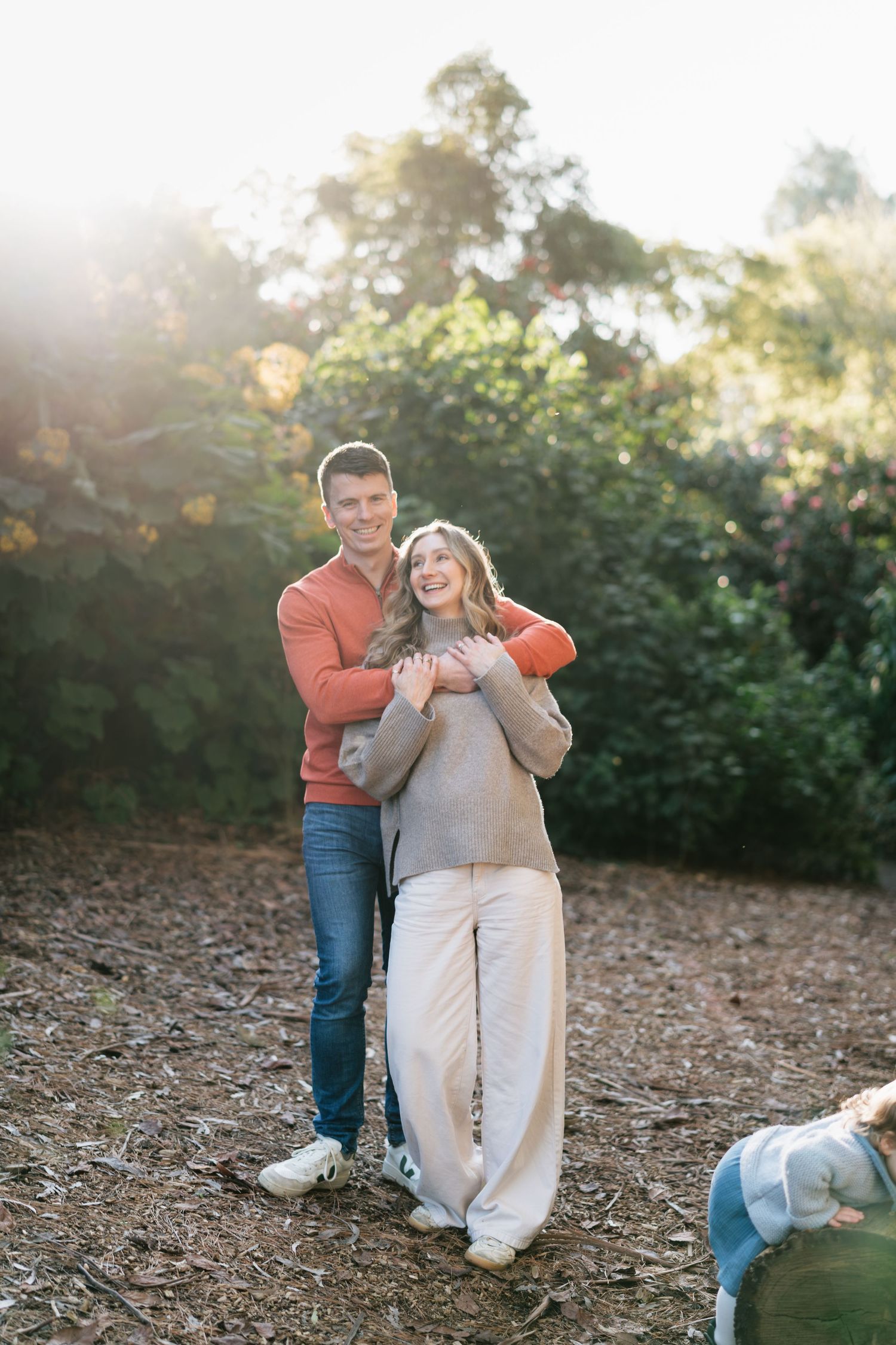 Happy couple embracing in golden sunlight surrounded by lush green trees outdoors.