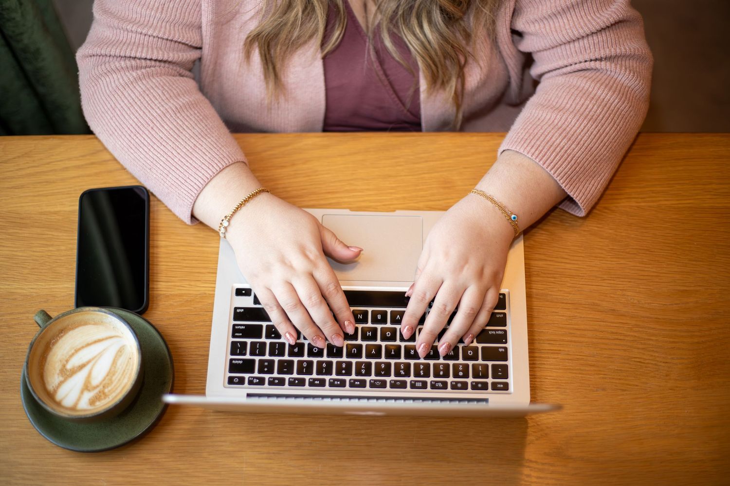 Overhead view of hands typing on laptop keyboard with coffee cup on wooden desk.