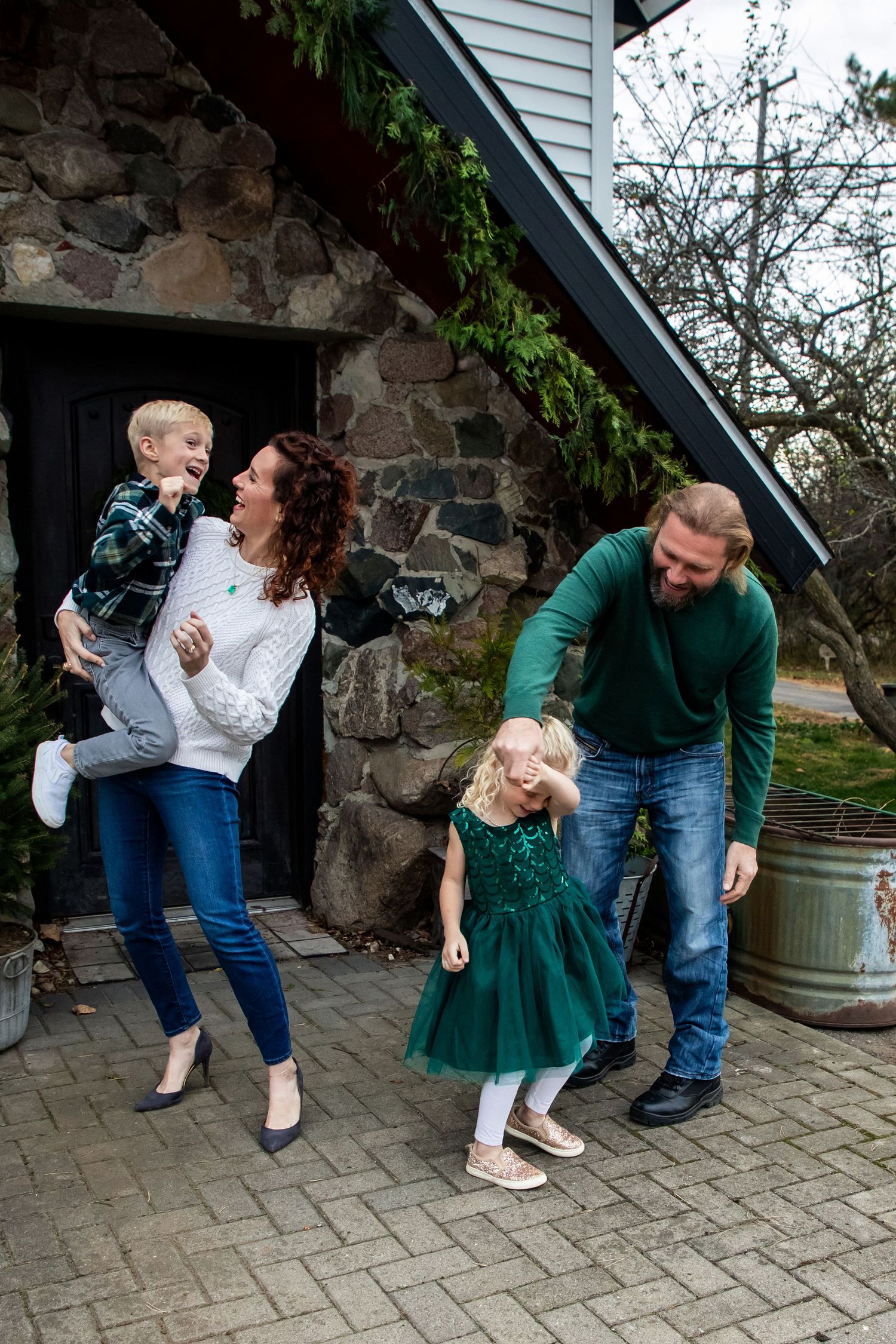 Playful family photo session on stone patio with white house and greenery backdrop.
