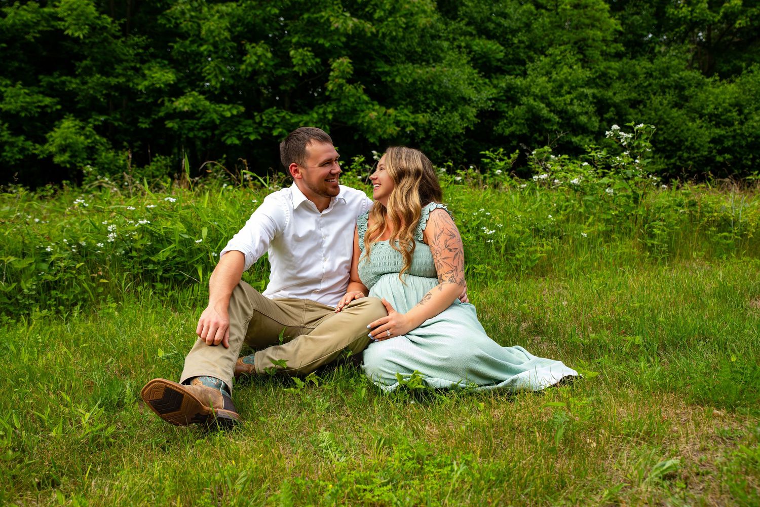 Couple lounging on blanket in lush green summer meadow during outdoor photo session.