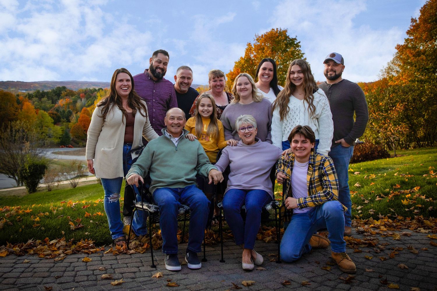 Multi-generational family group photo in autumn setting with fall foliage.