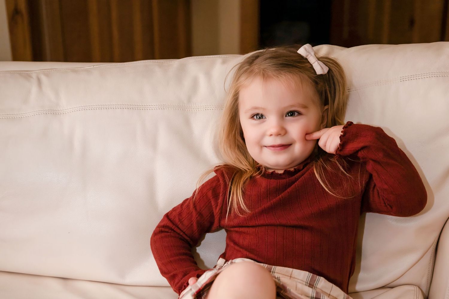 Child in burgundy sweater playing and making expressions on white couch.