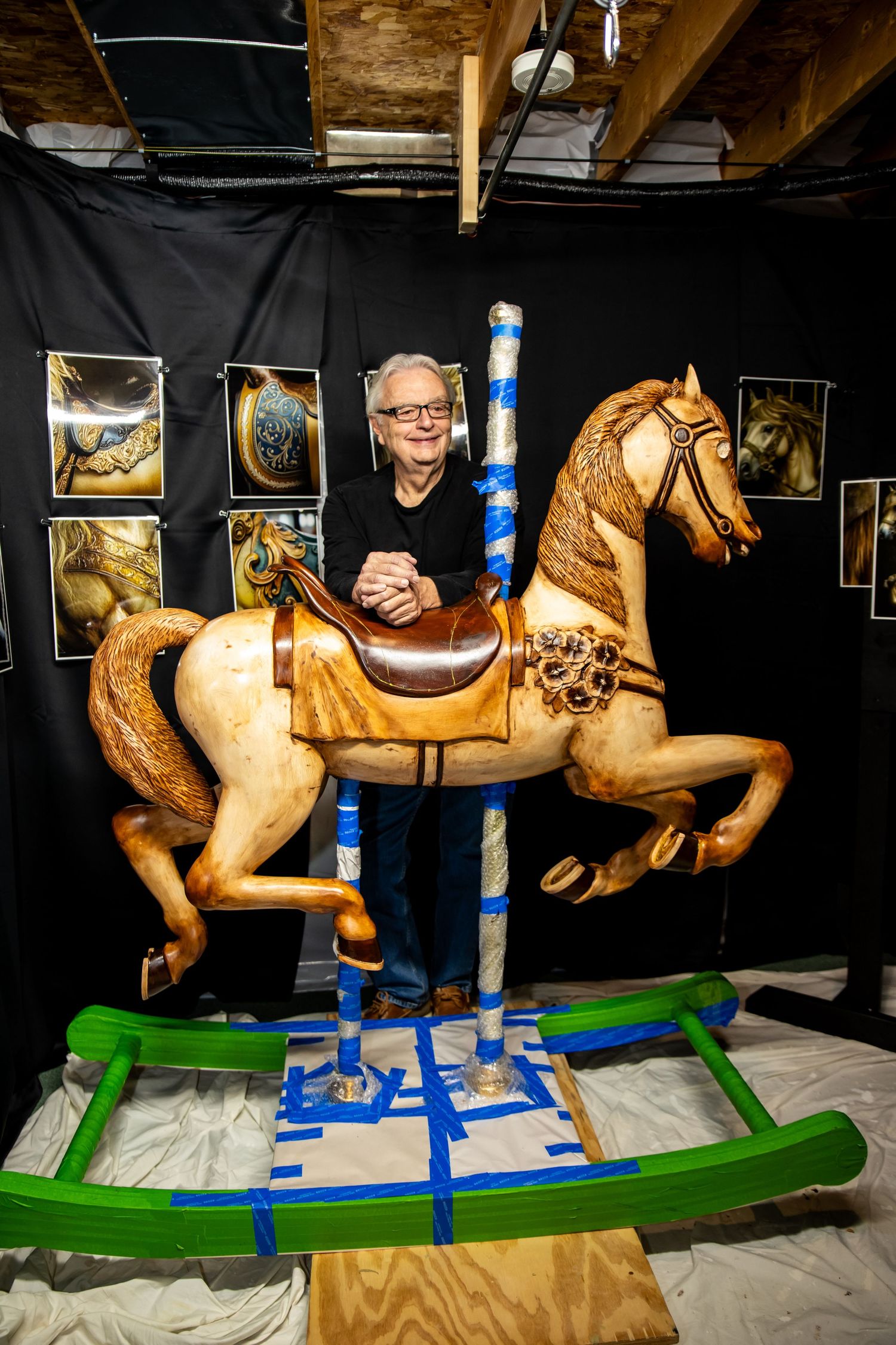 Vintage carousel horse restoration project with wooden horse on green and blue supports against dark background.