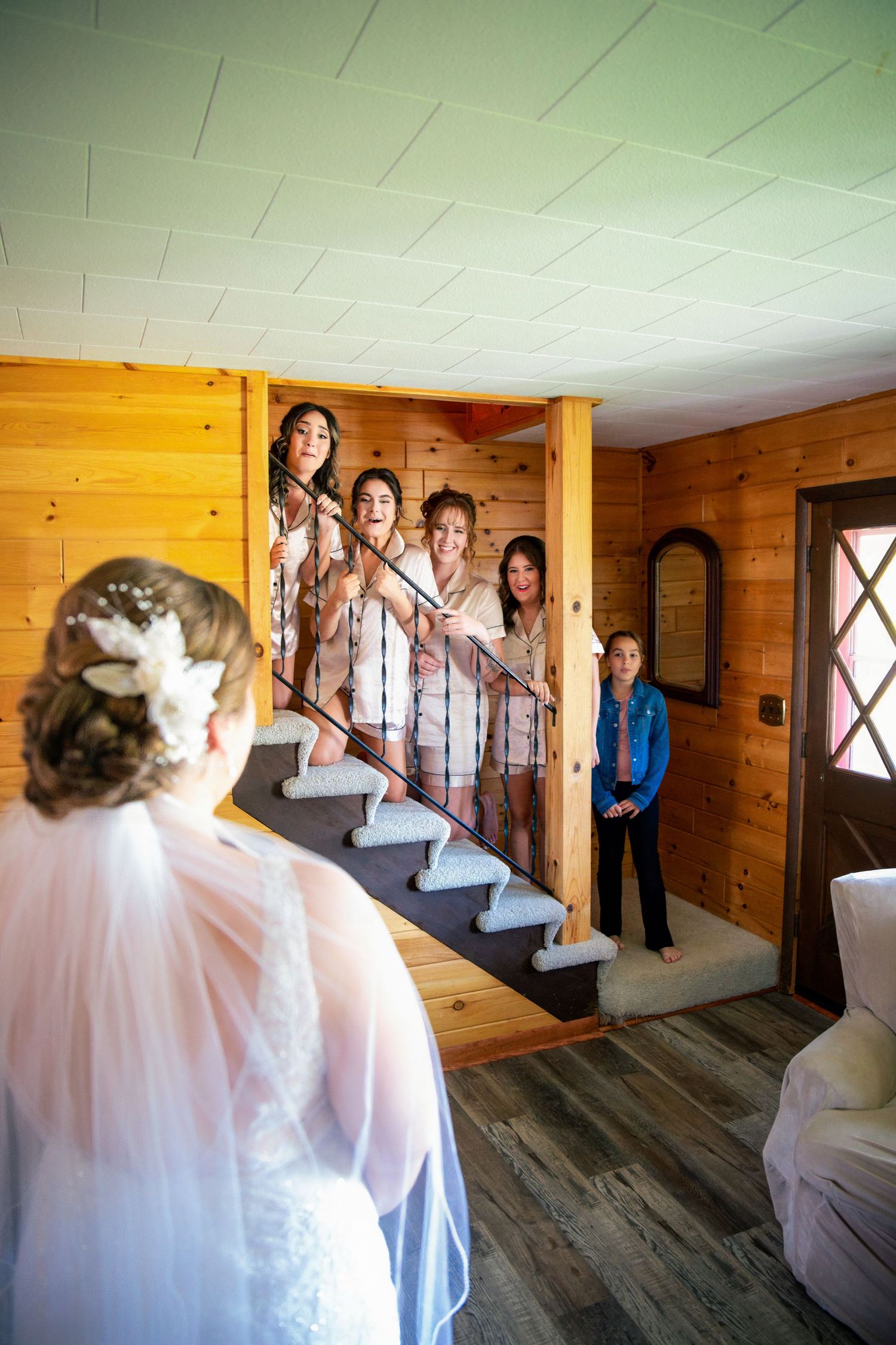 A group gathers on wooden stairs inside a rustic cabin with pine walls and a white ceiling.