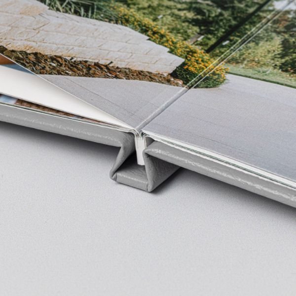 Close-up of a photo book spine with a silver binding clip, showcasing layered pages and a nature photograph on the cover.