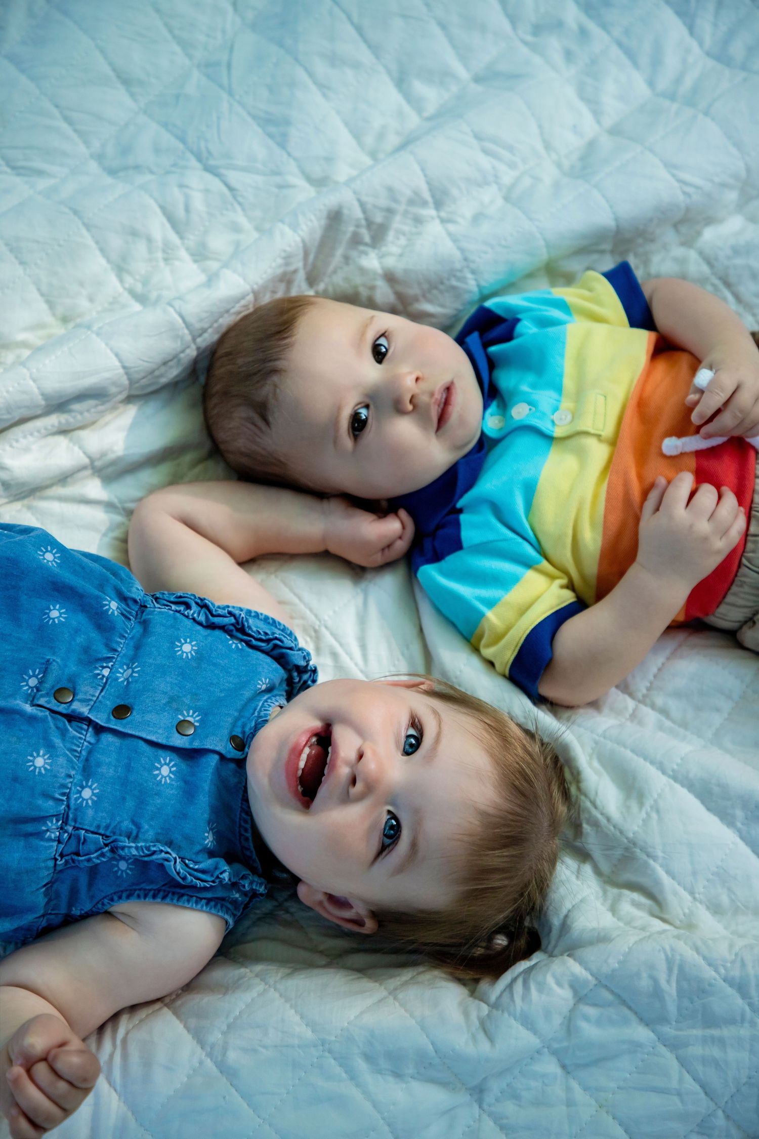Young child wearing colorful outfit lying on blue quilted blanket.