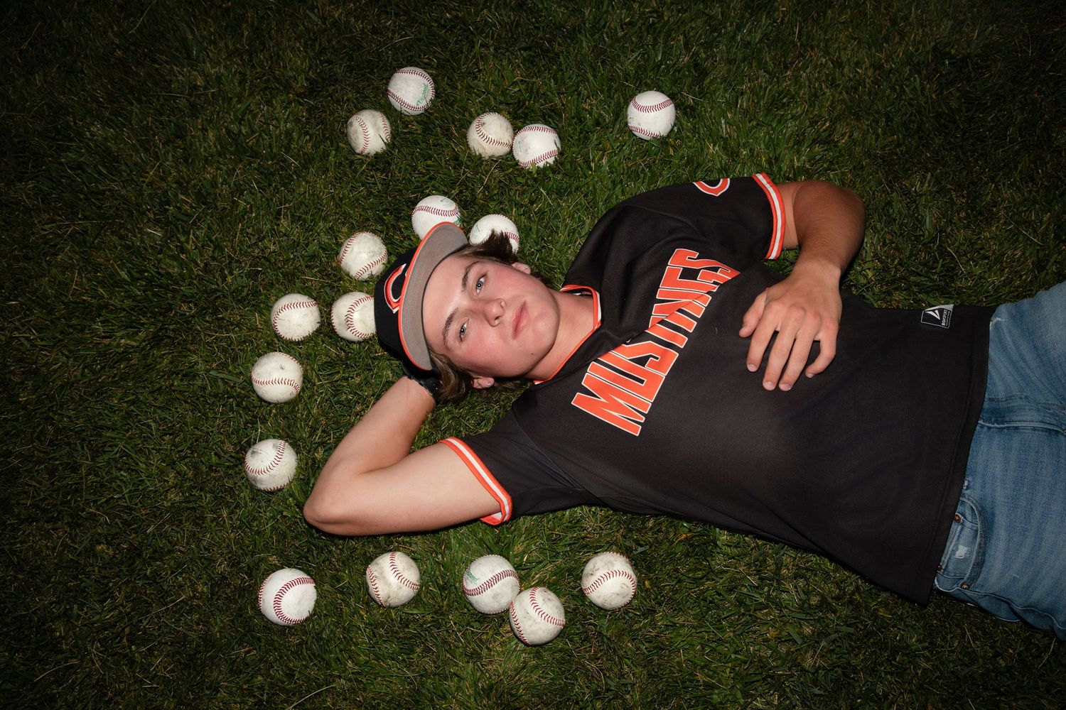 Person lying on grass surrounded by scattered baseballs.