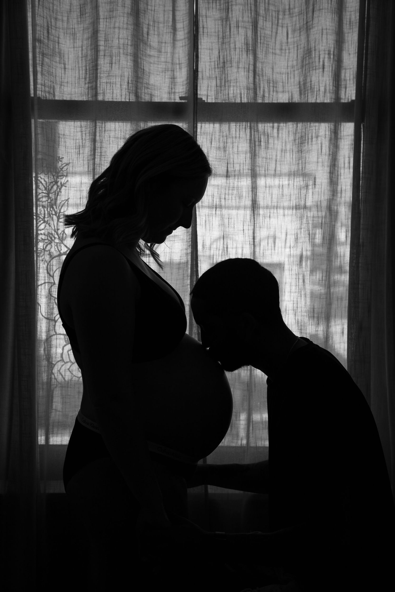 Silhouetted figures create a romantic sequence against a backlit window with sheer curtains.