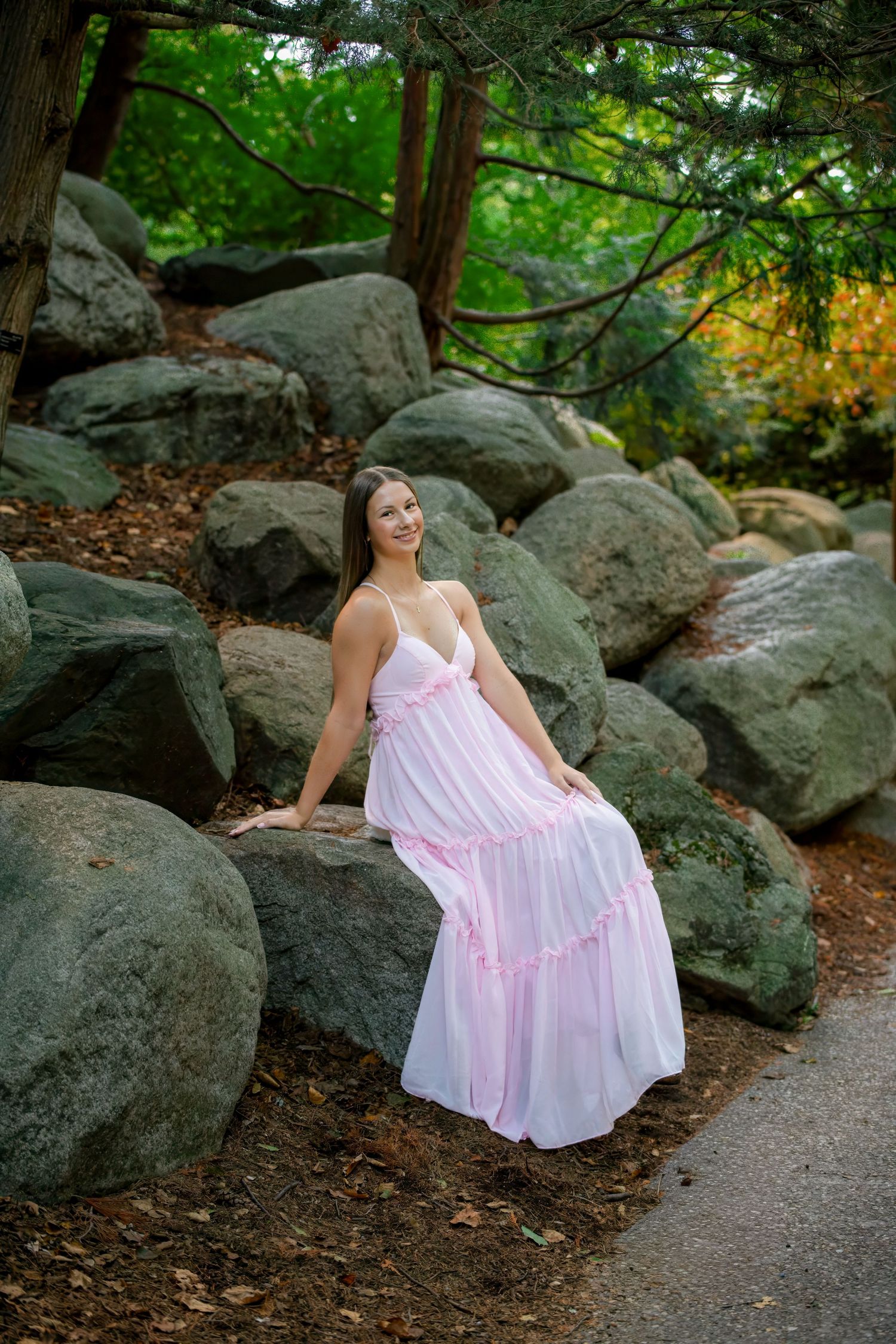 Person in pink maxi dress poses on large rocks in wooded setting.