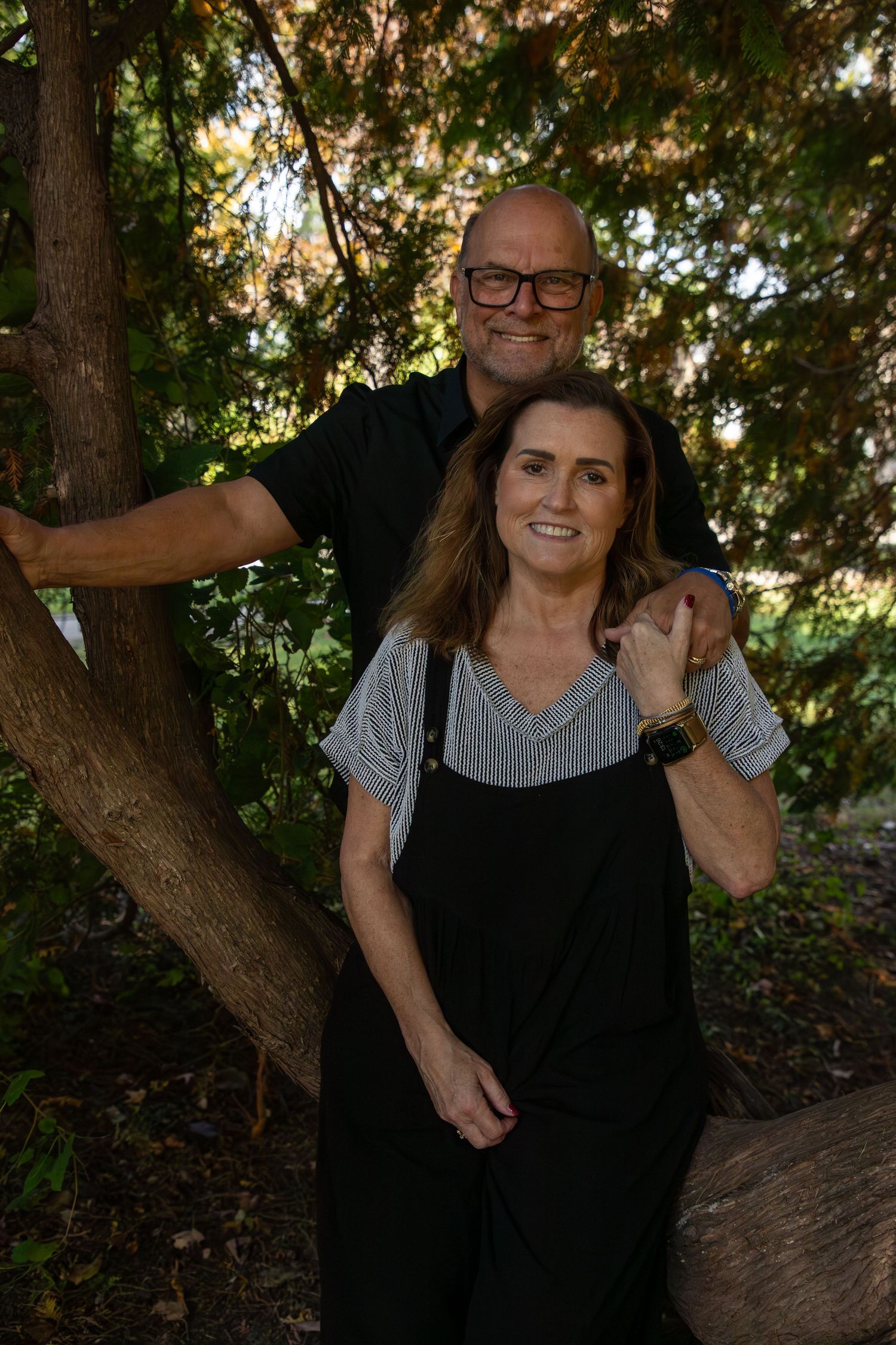 Couple sharing playful moments among trees in dappled sunlight.