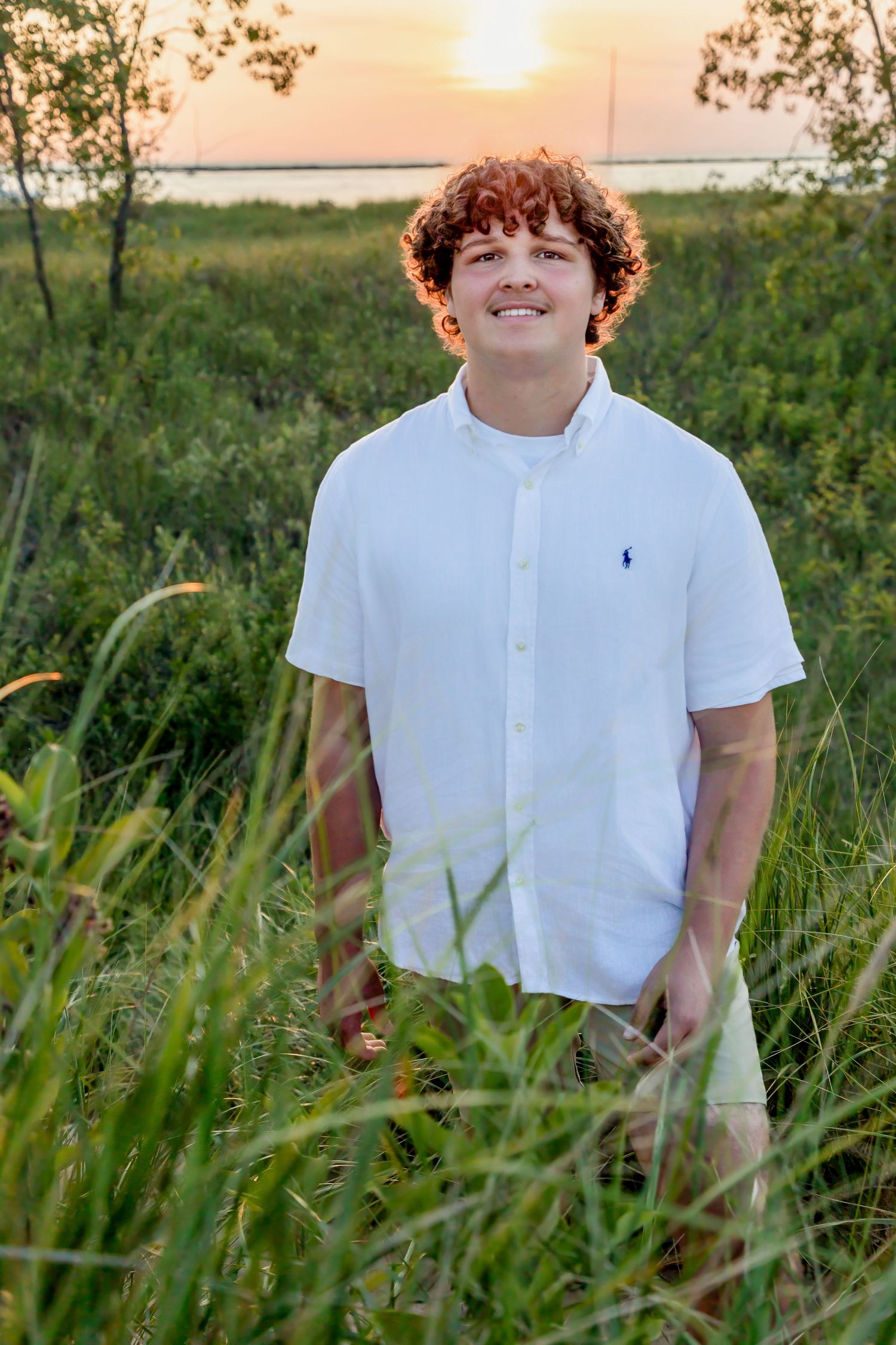 Young person in white shirt walking through tall grass at sunset.
