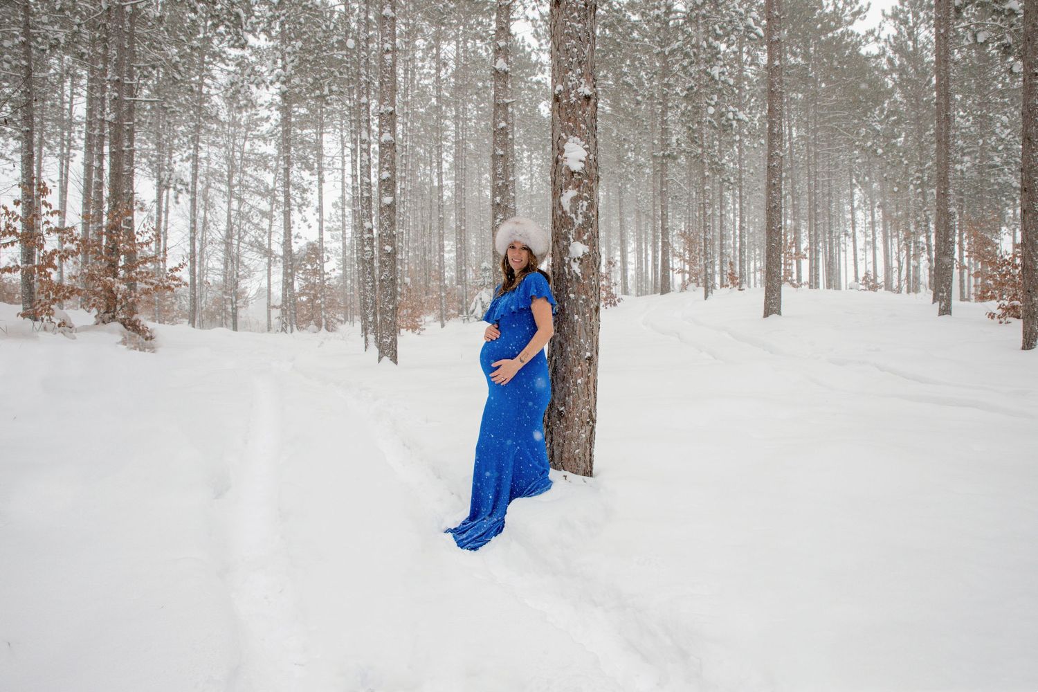 Person in bright blue outfit standing in snowy winter forest.
