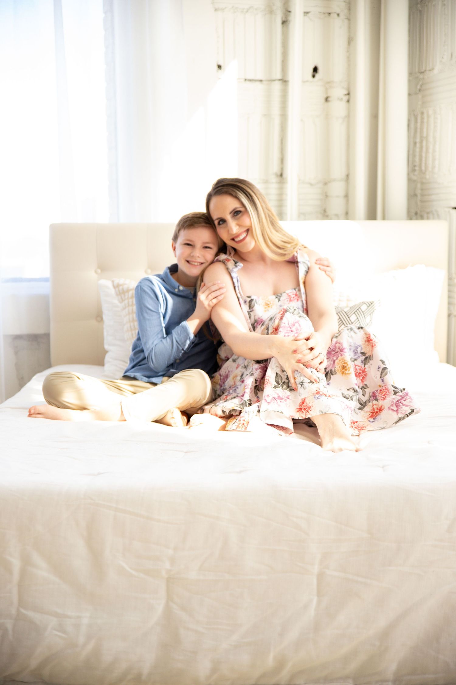 Intimate indoor lifestyle photography session with soft white bedding and floral dress.
