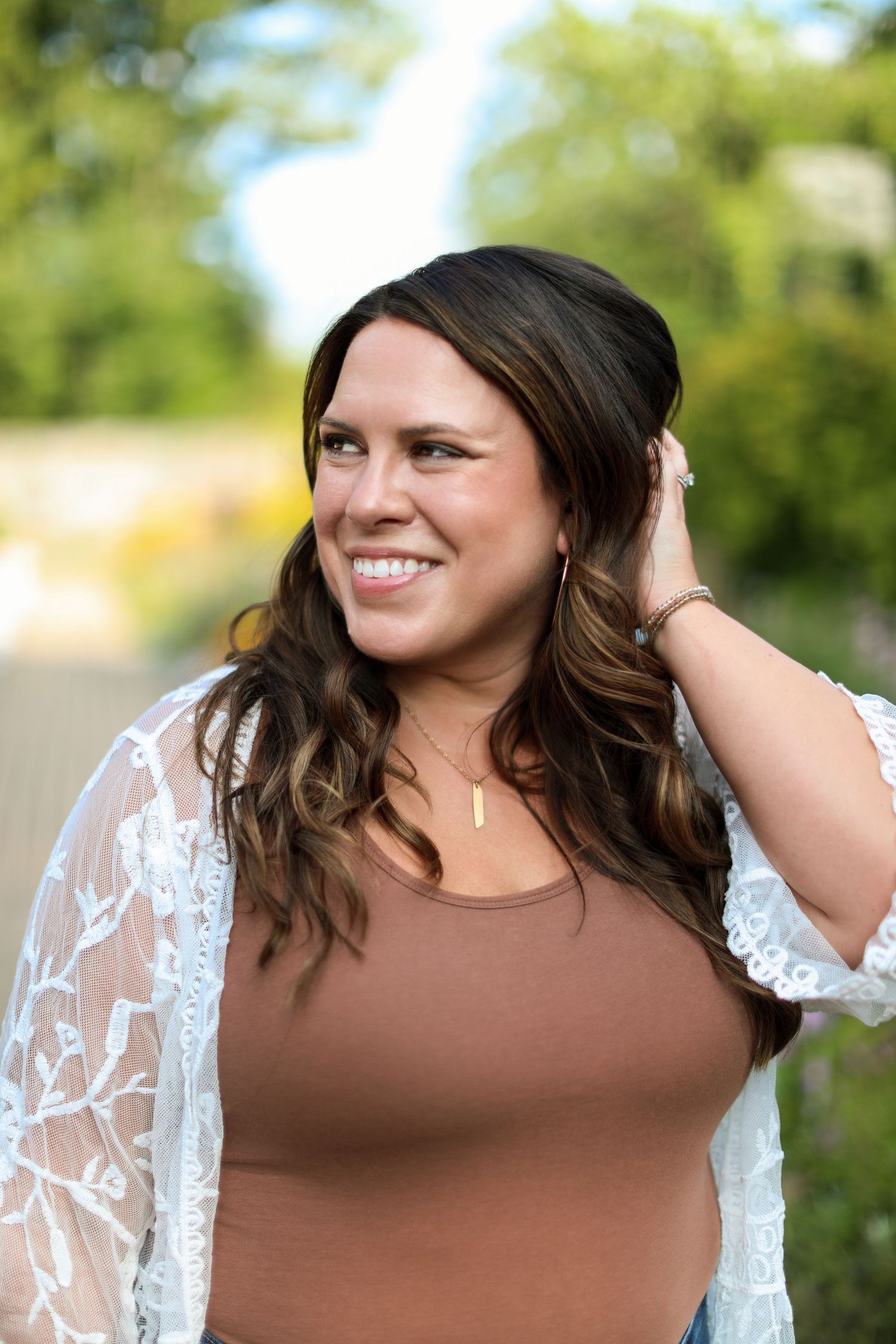 Outdoor portrait session wearing brown top and white lace kimono against natural greenery.