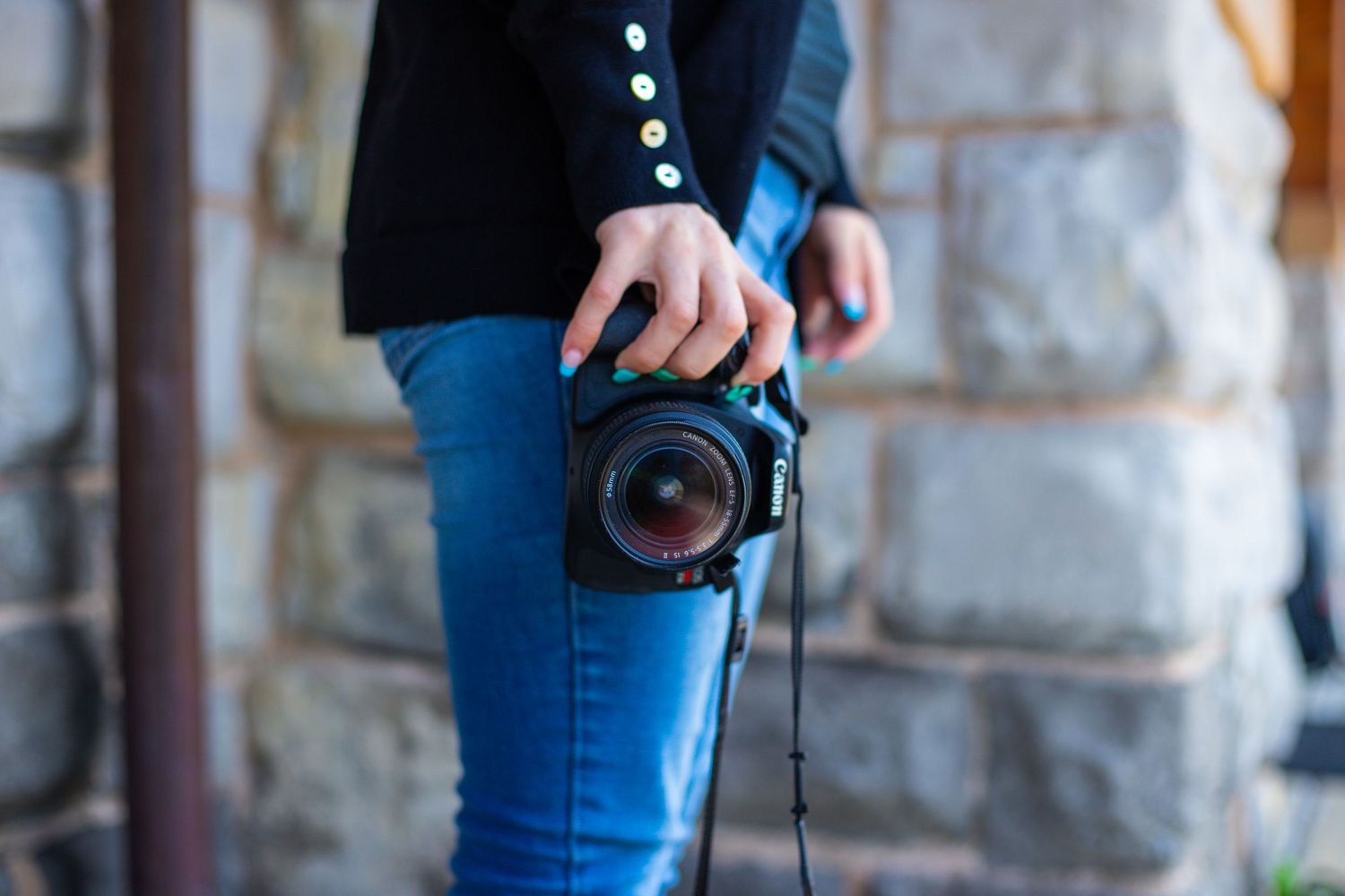 Close-up of hands holding professional camera wearing blue jeans.